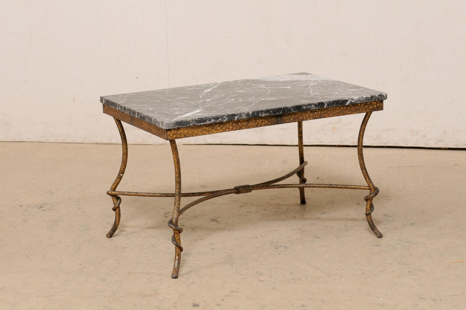 A Spanish marble-top coffee table from the mid 20th century. This vintage table from Spain has a rectangular-shaped marble top, which rests atop a hammered iron frame. The underside of this table is open and airy. The four thin, rounded legs are set