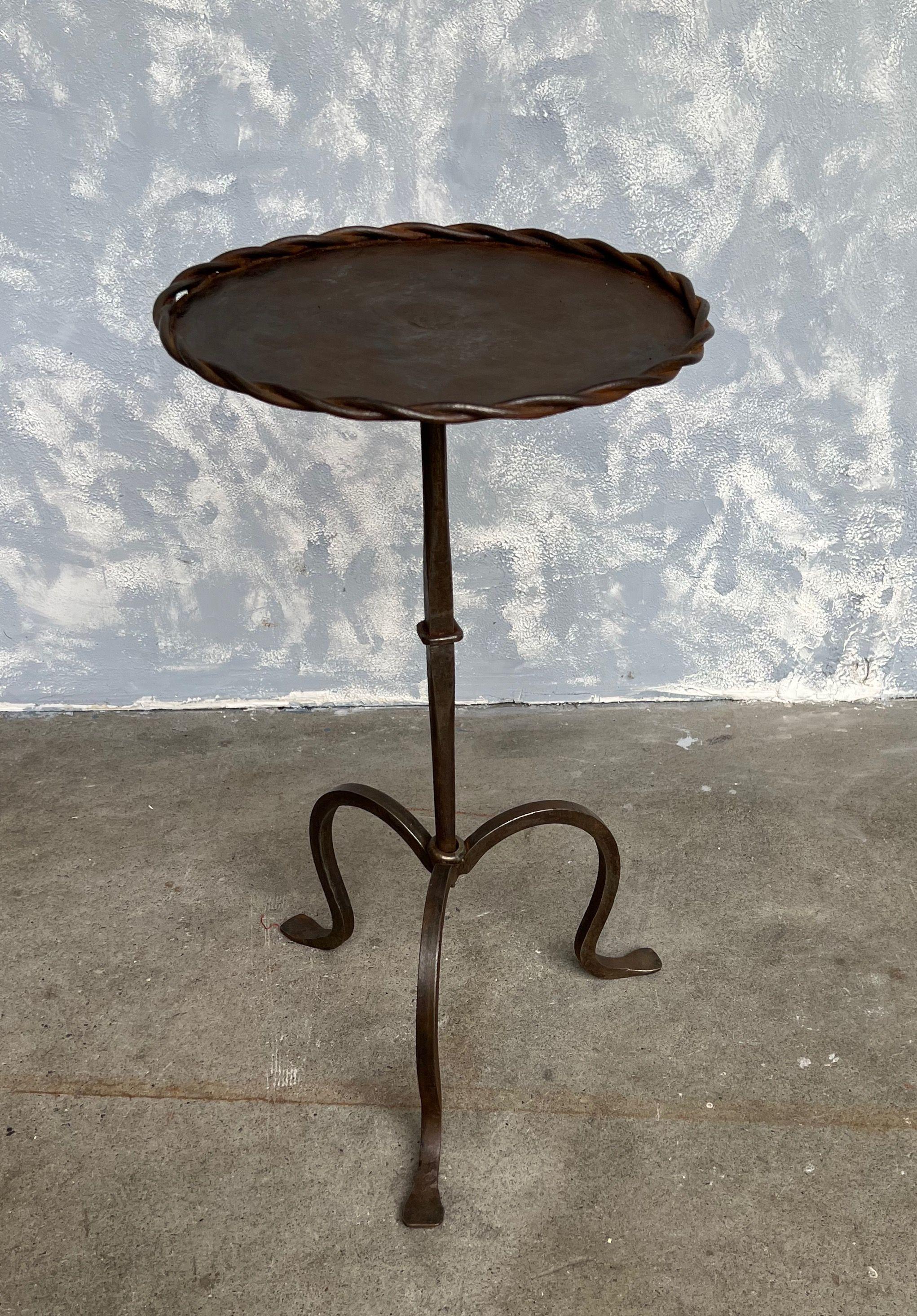 Small iron and metal end table with a tripod base, a central ring detail on the stem, and a braided surround at the top. Perfect for a drink, it can easily be moved around as needed. Beautiful bronzed patina. 

Spanish, 1950s. Very good vintage