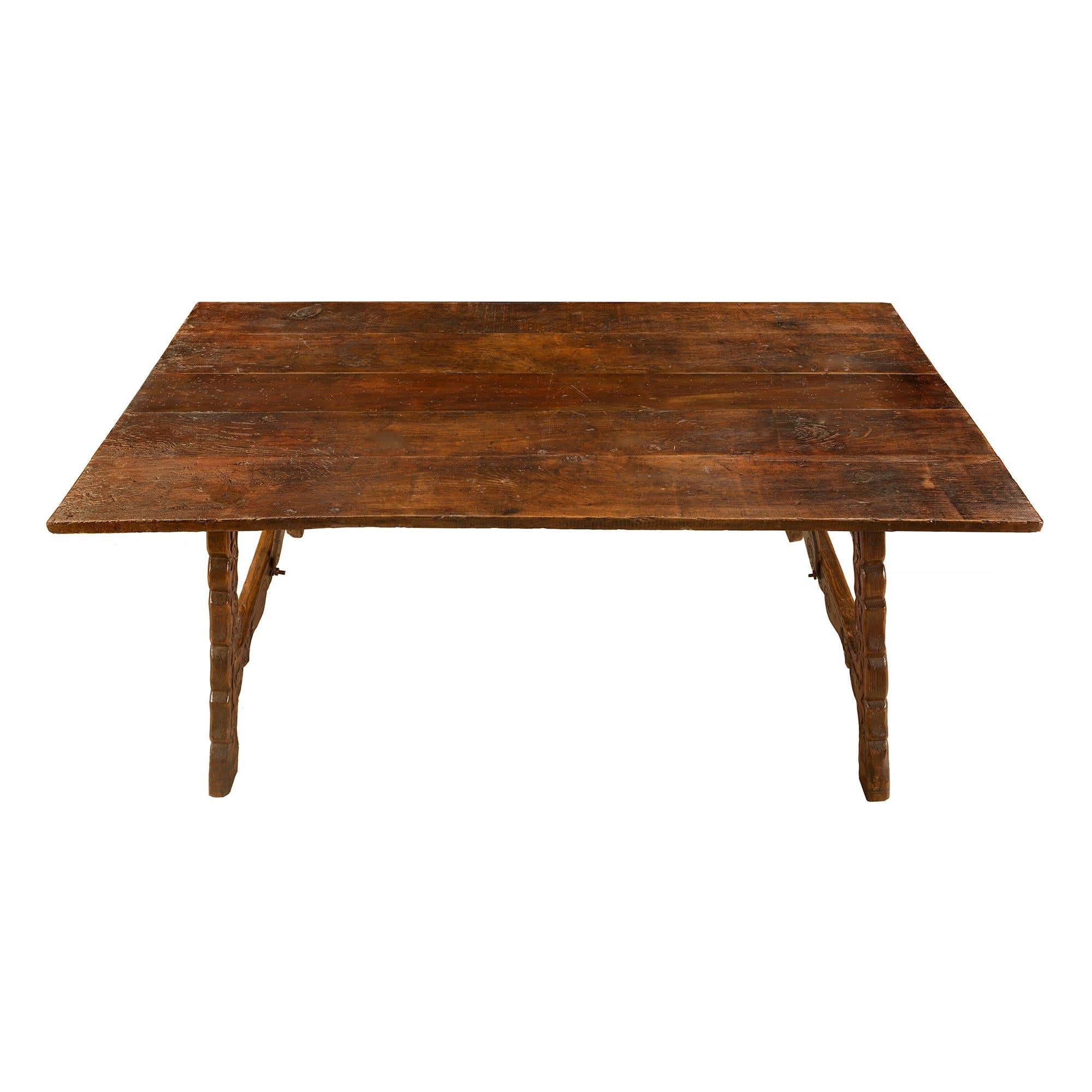 A handsome Spanish mid 19th century Country dining / center table in dark patinated oak. The impressive inclined table supports are decorated with scrolled carved leaves and acorn garlands. Joined by the original 'S' scrolled wrought iron