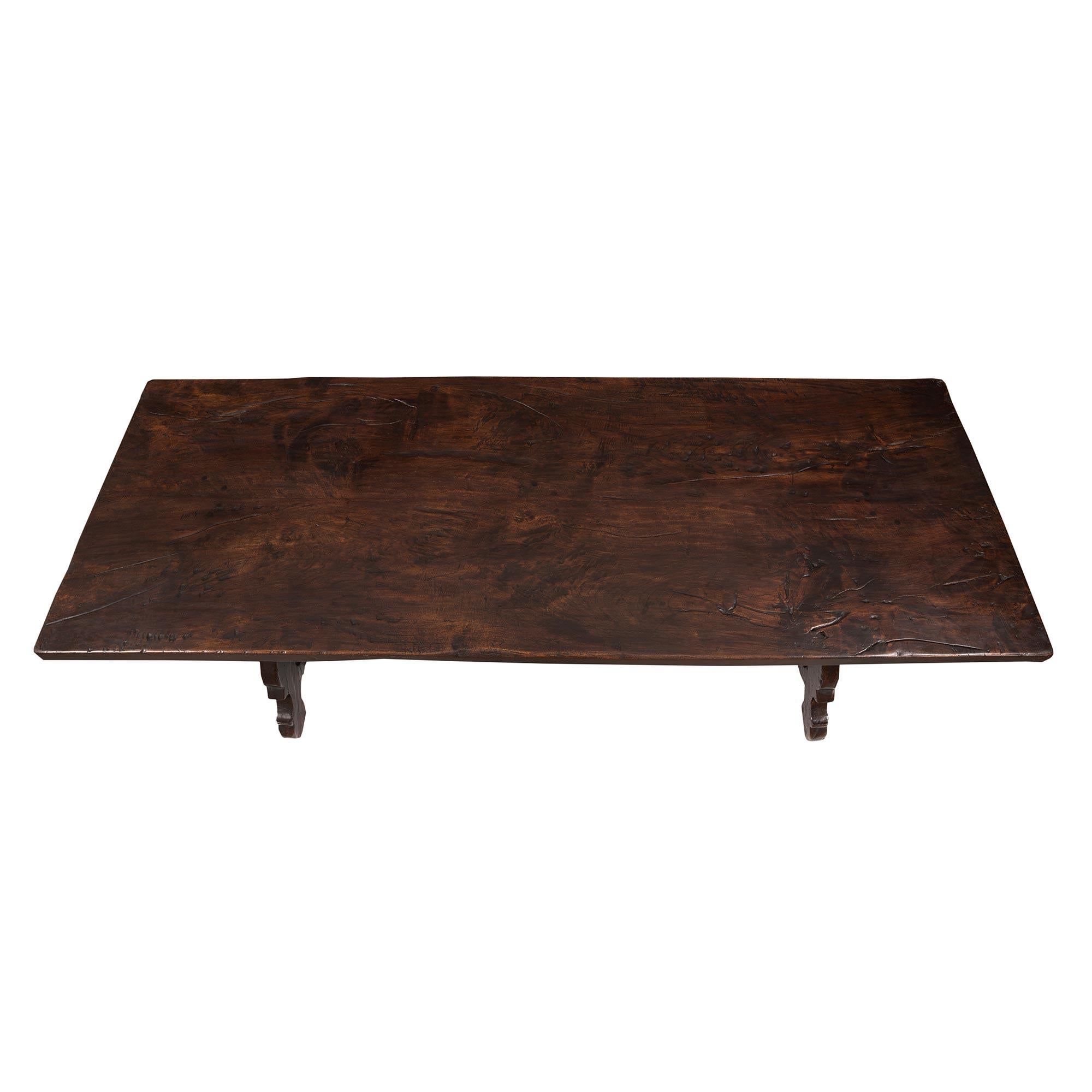 A handsome Spanish mid-19th century Country style dark oak trestle dining/center table. The table is raised by most decorative finely scrolled slanted supports at each side connected by the striking original hand beaten wrought iron interlocking