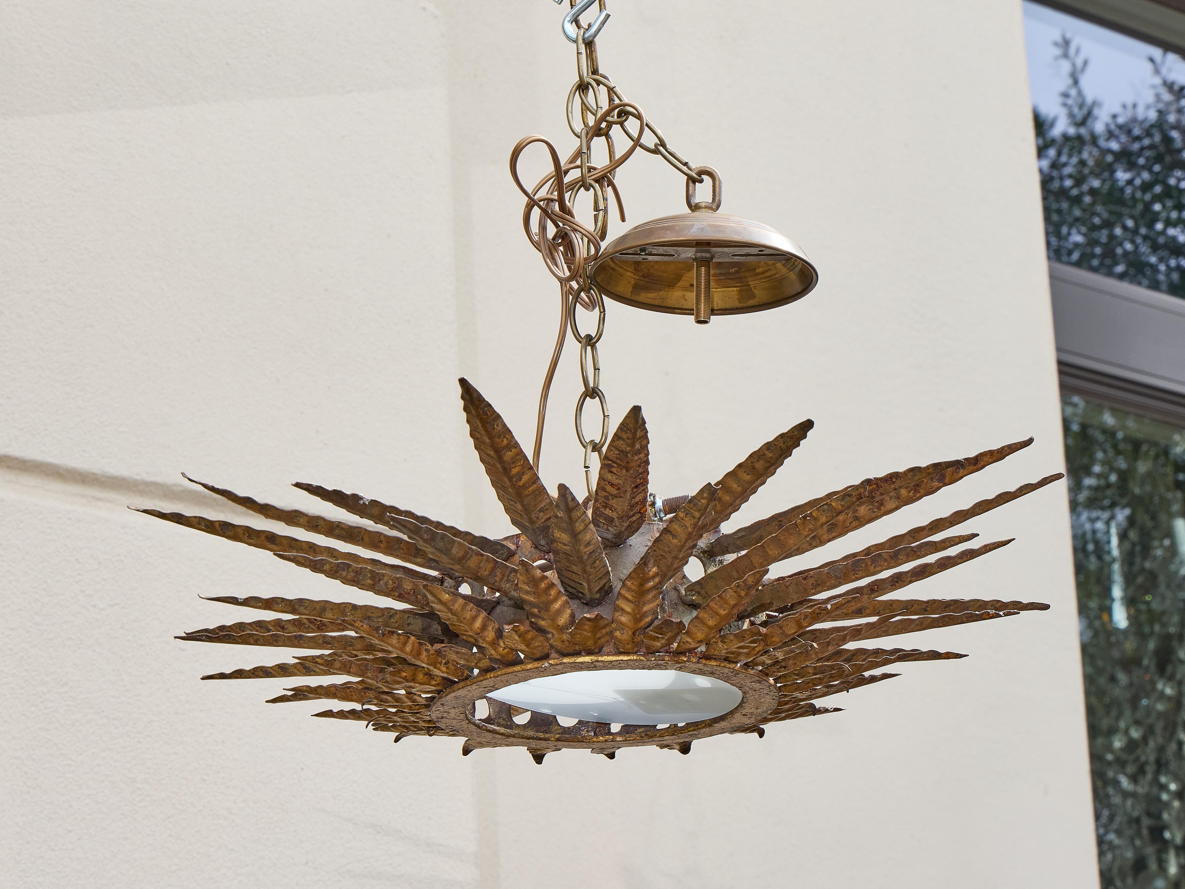 Un'imponente lampada a raggiera del Medioevo spagnolo, realizzata in metallo dorato e martellato con una presenza scultorea di grande effetto. La forma a raggiera si ispira alle foglie di agave o a motivi botanici stilizzati, con elementi