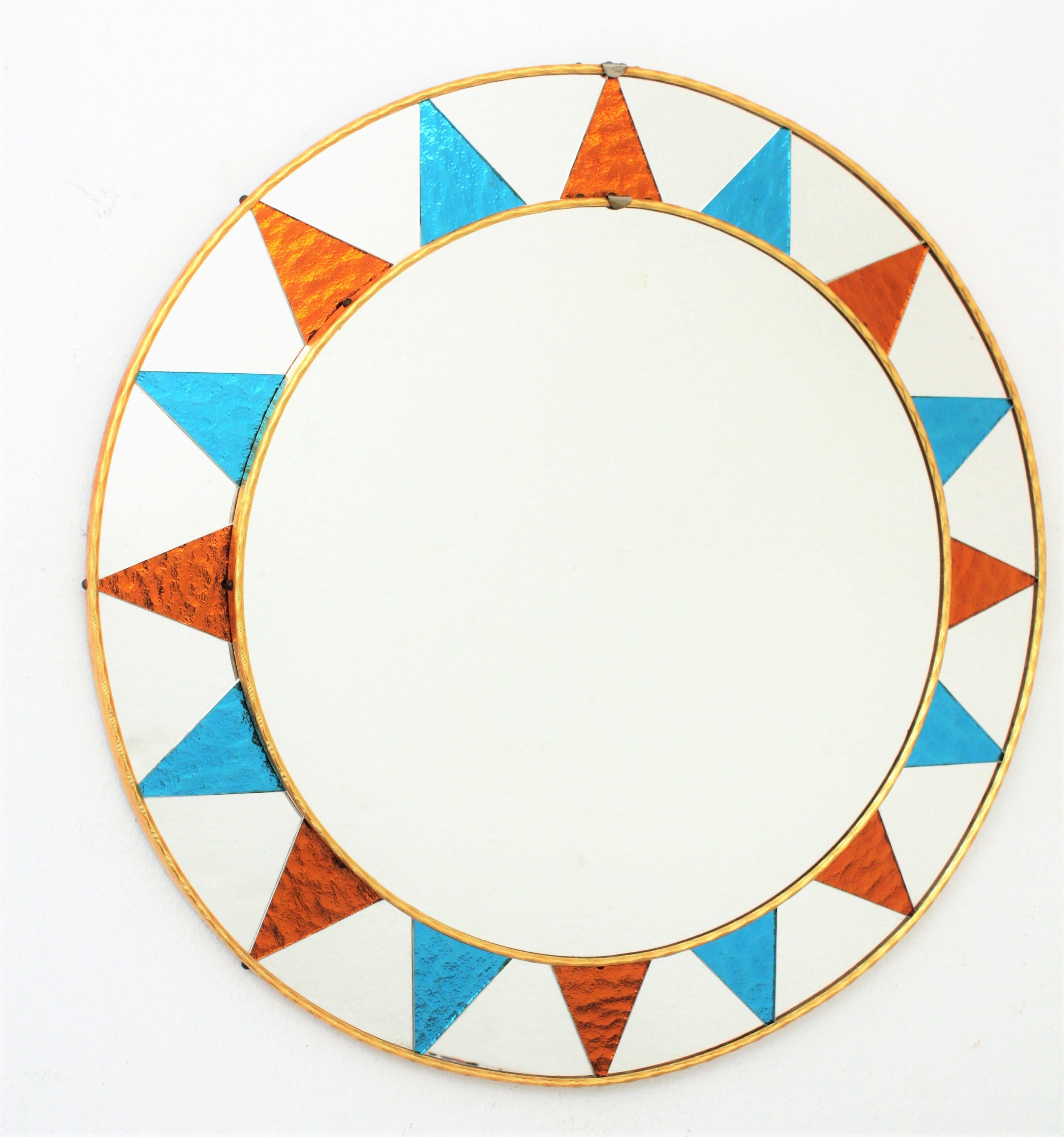 A highly decorative Mid-Century Modern circular mirror with a frame composed by pieces of glass mirrors, and textured mirrored glass rays in blue and orange colors distributed creating a sunburst pattern. Spain, circa 1960s. 
Overall diameter: 59 cm