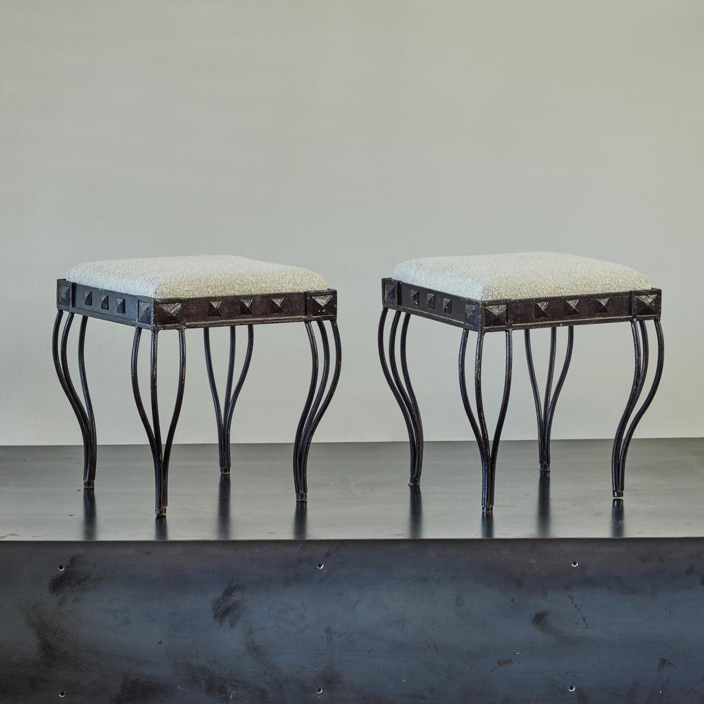 Pair of artisanal Spanish mid-century cast iron stools. Featuring minimalist three-wired legs in a slender, tapered Neo-Classical shape, the set is replete with surprising contrast. The frieze is trimmed with chunky, pyramid-shaped studs, atop which