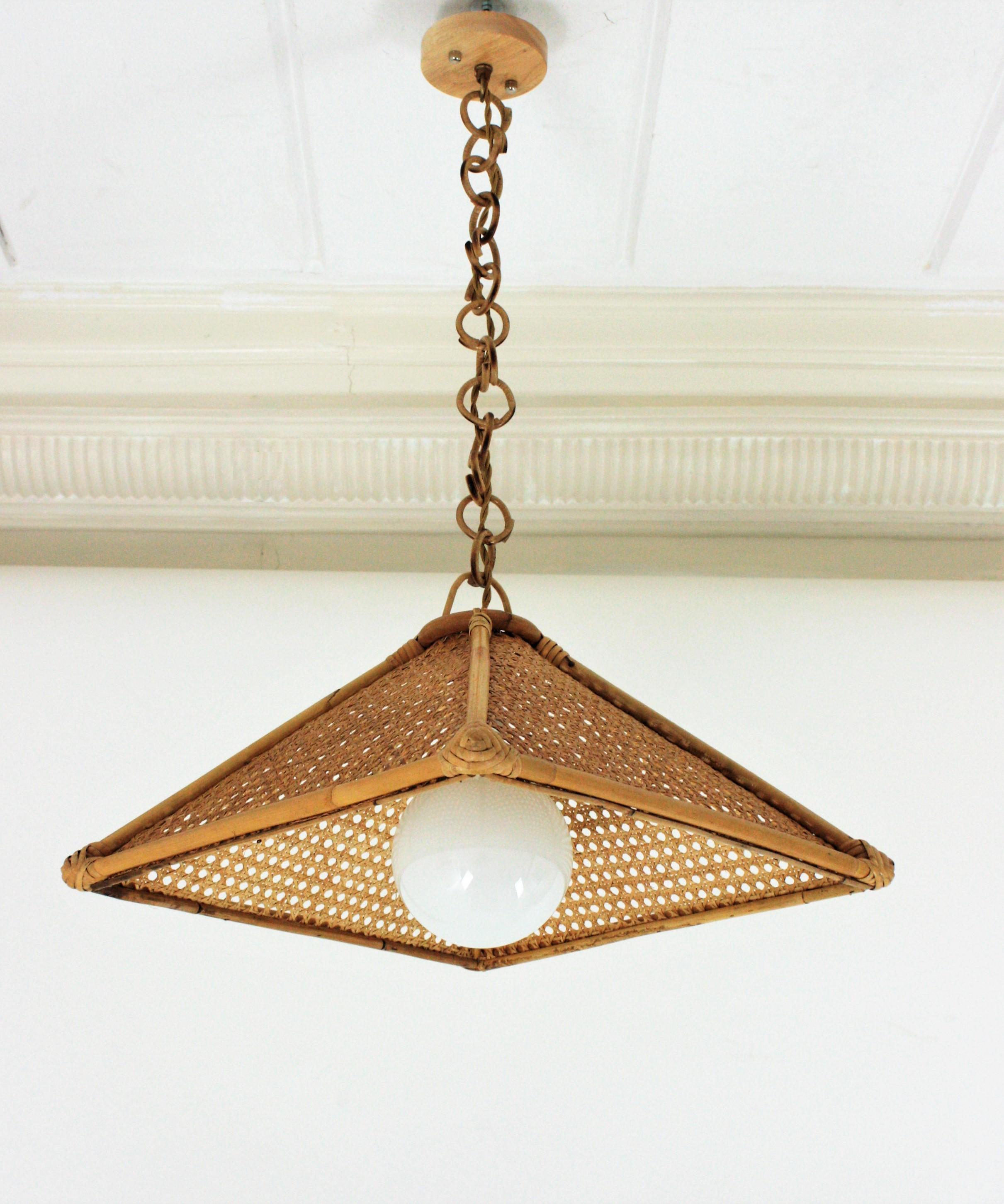 Mid-Century Modern Woven Cannage and Rattan Pendant Lamp / Chandelier. Spain, 1960s
This beautiful suspension lamp features a trapezoid rattan structure with wicker wire panels. It hangs from a chain with round rattan links topped by a wooden