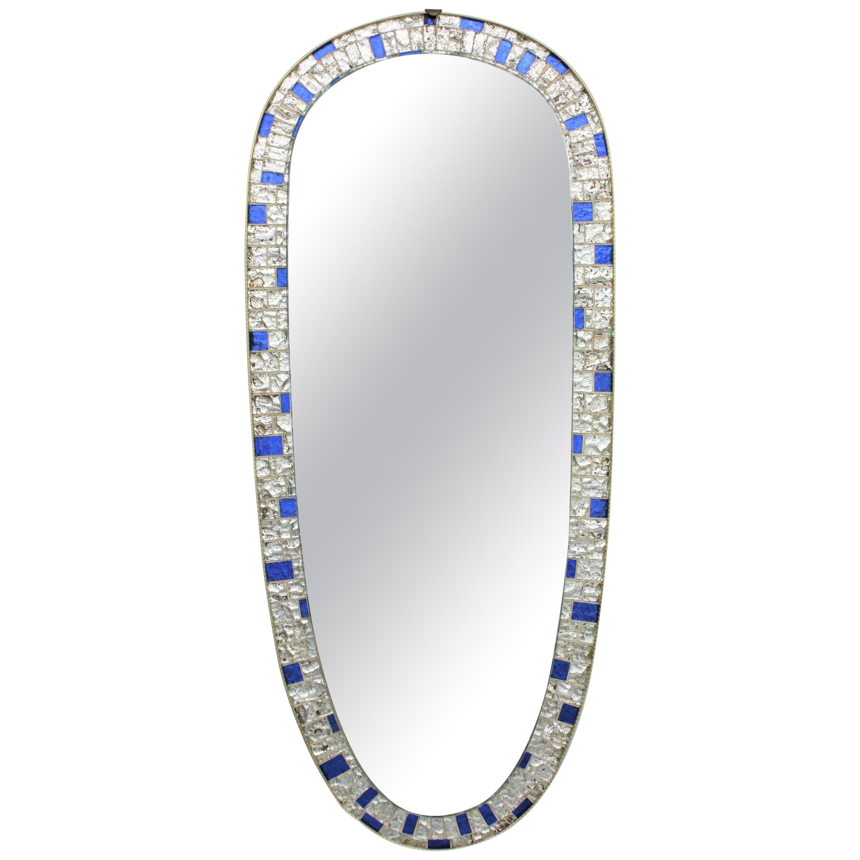 A Mid-Century Modernist oval wall mirror with mosaic frame in blue and silver colors, Spain, 1960s
This eye-catching mirror is framed by handcut clear and blue iridescent textured glasses. The silver leaf under the glasses provides an iridescent