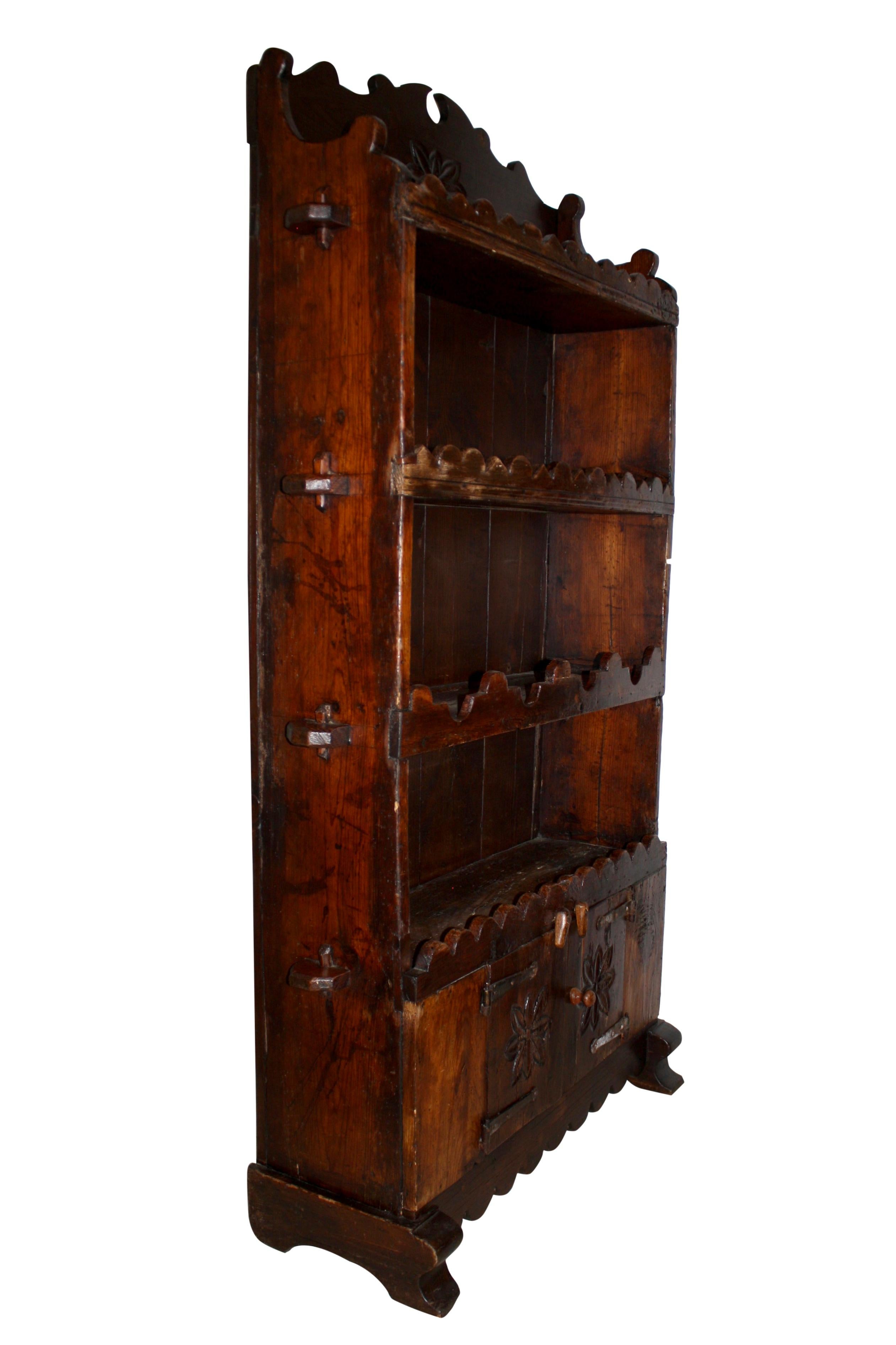 Comprised of four shelves with decorative trim and tusk tenon joinery, a two-door cabinet with long iron hinges, a broken pediment, and hand carved flowers, this oak bookcase brings a rustic, Old World charm to any room. The top three shelves have