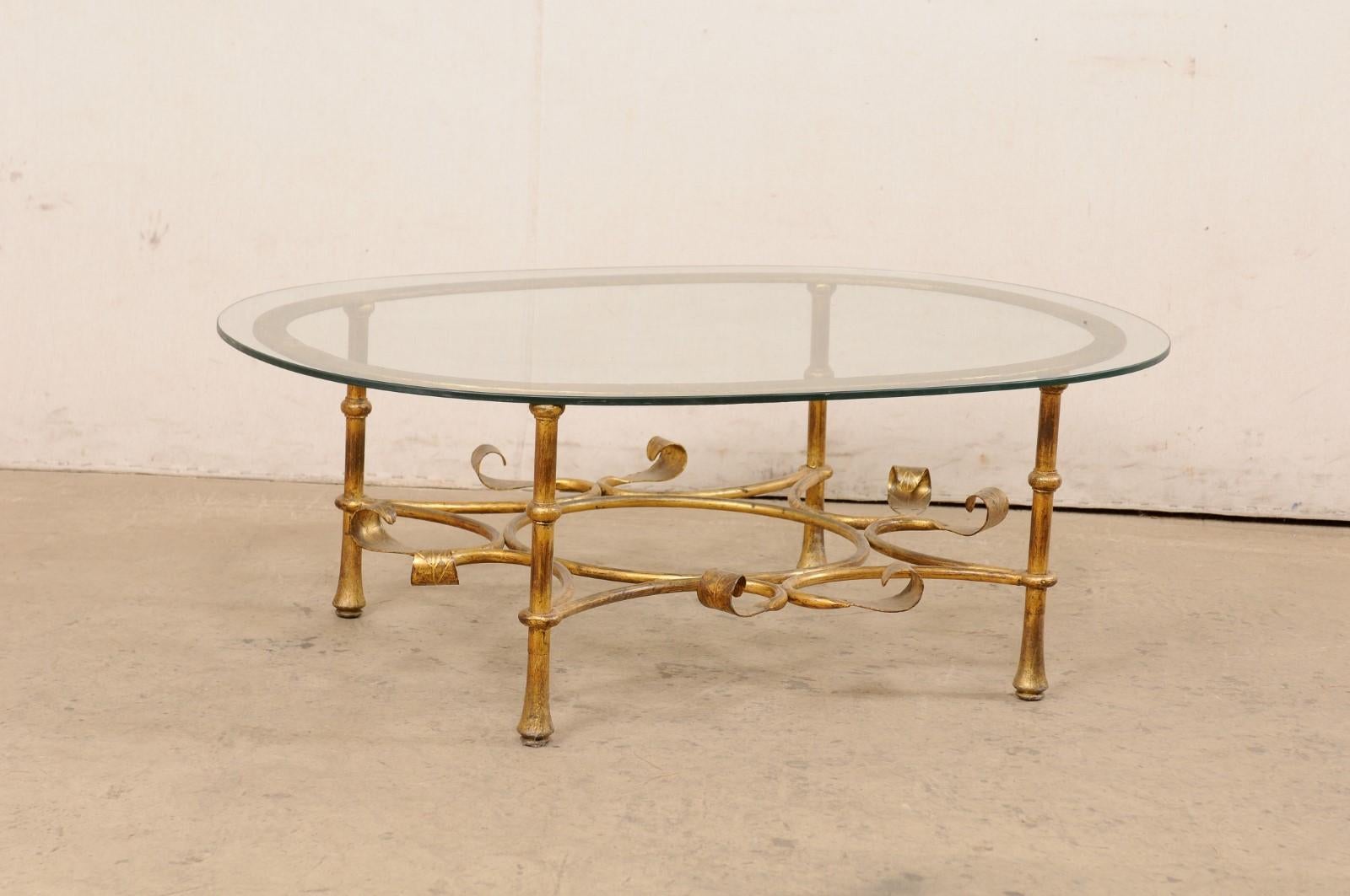 A Spanish iron base coffee table with glass top from the mid 20th century. This vintage table from Spain features an oval-shaped glass top, which is raised upon an iron frame comprised of a oval top raised upon four rounded legs. Each leg is braced