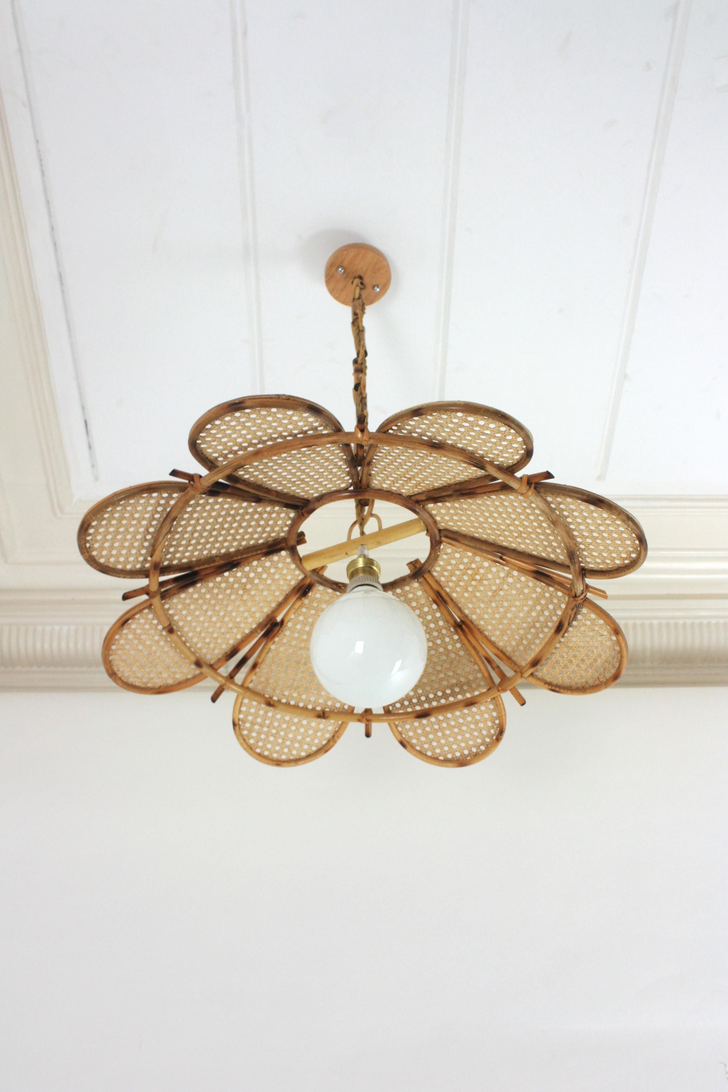 Flower Shaped Rattan Ceiling Pendant, Large Size. Spain, 1960s
This large pendant has an eye-catching flower design featuring 4 layered rattan petals joining between them as a flower.
It hangs from a chain with round rattan links ended by a wooden