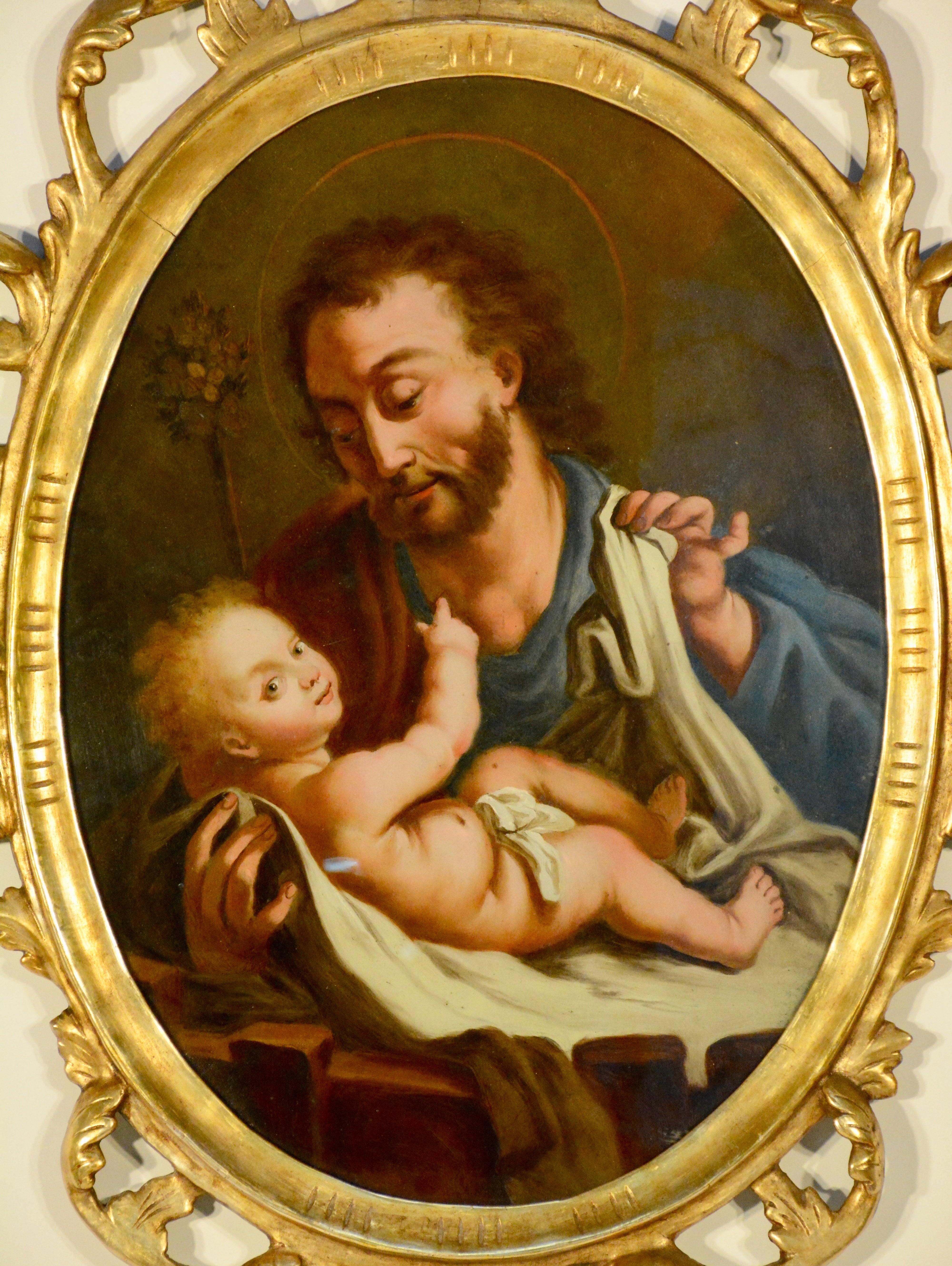 This painting is from Northern Spain of a religious reverse painting on glass depicting Saint Joseph with the Christ Child. It is enclosed by an arched, gilded wood and gesso frame and carved with open work detail. Painting measures 15.75
