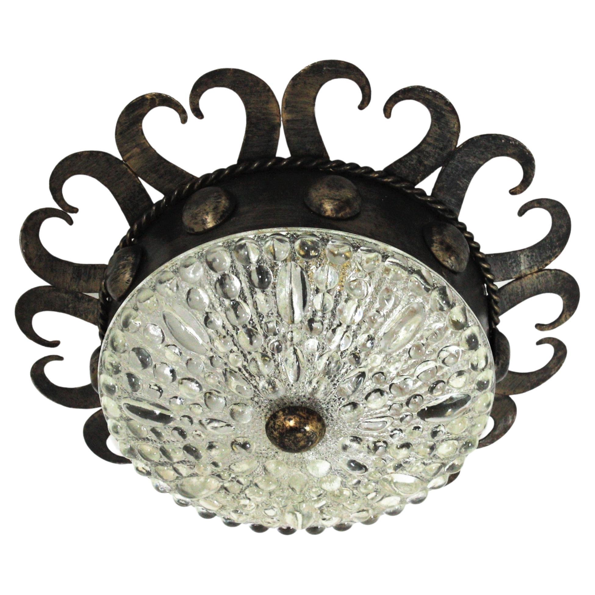 Eye-catching iron and glass crown flush mount with scrolled and ball details, Spain, 1950s.
This light fixture has an interesting design combining scroll and geometric accents. The patinated iron frame has sunburst disposition and scroll endings