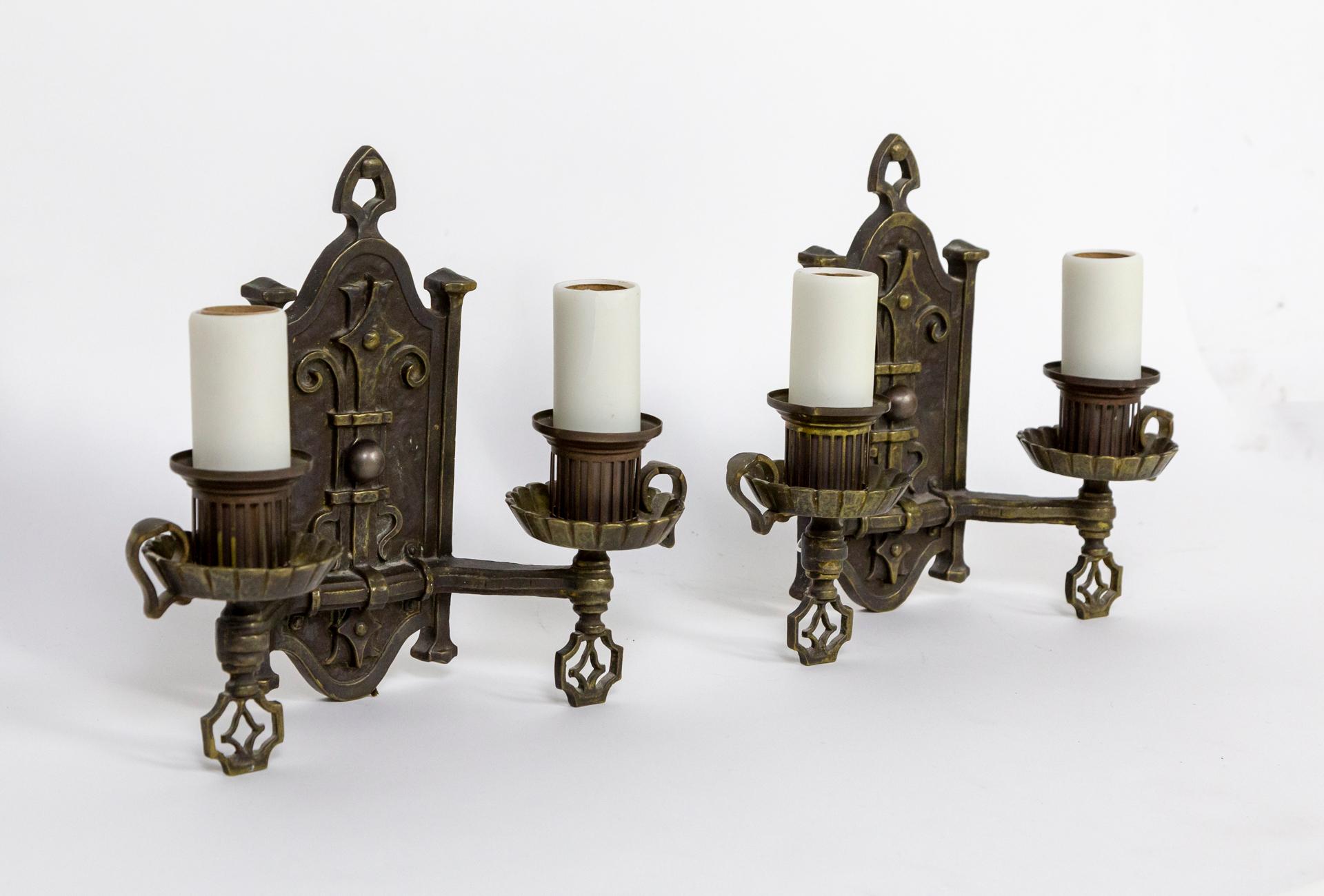 A finely cast and hammered, wrought iron pair of wall lights by Max Schaffer Co. circa 1930. Spanish Revival style and motifs with a lovely brass-bronze tone patina. Newly wired, new poly-resin candle covers. 2 medium base sockets. Stamped on the