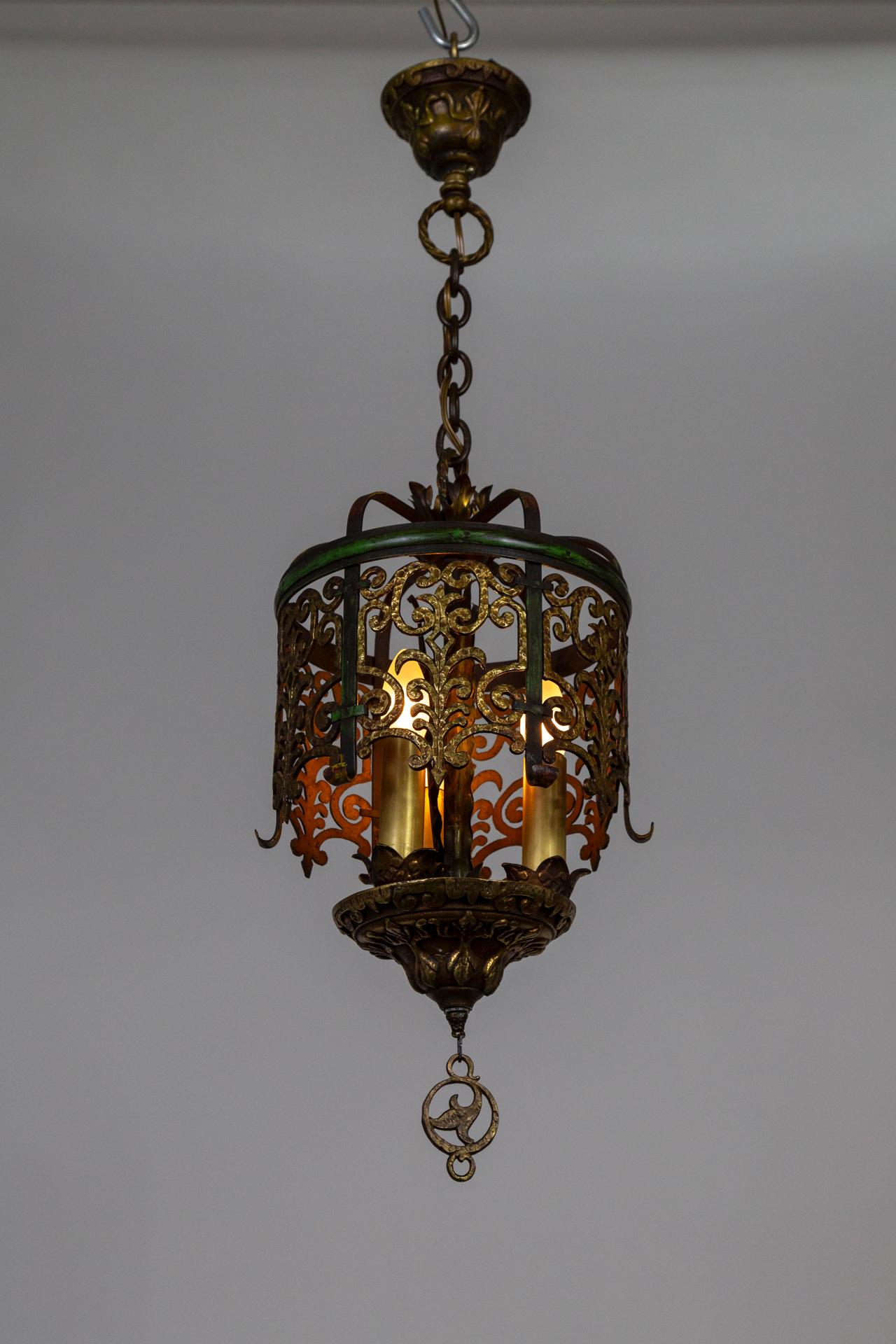 A unique, Medieval Revival chandelier with a touch of 1920s Nouveau. The structure has a rich, antique brass tone with green and red accents. Nicely proportioned, with detailed, heavy, casted canopy and bottom bowl. Three candlestick lights (medium