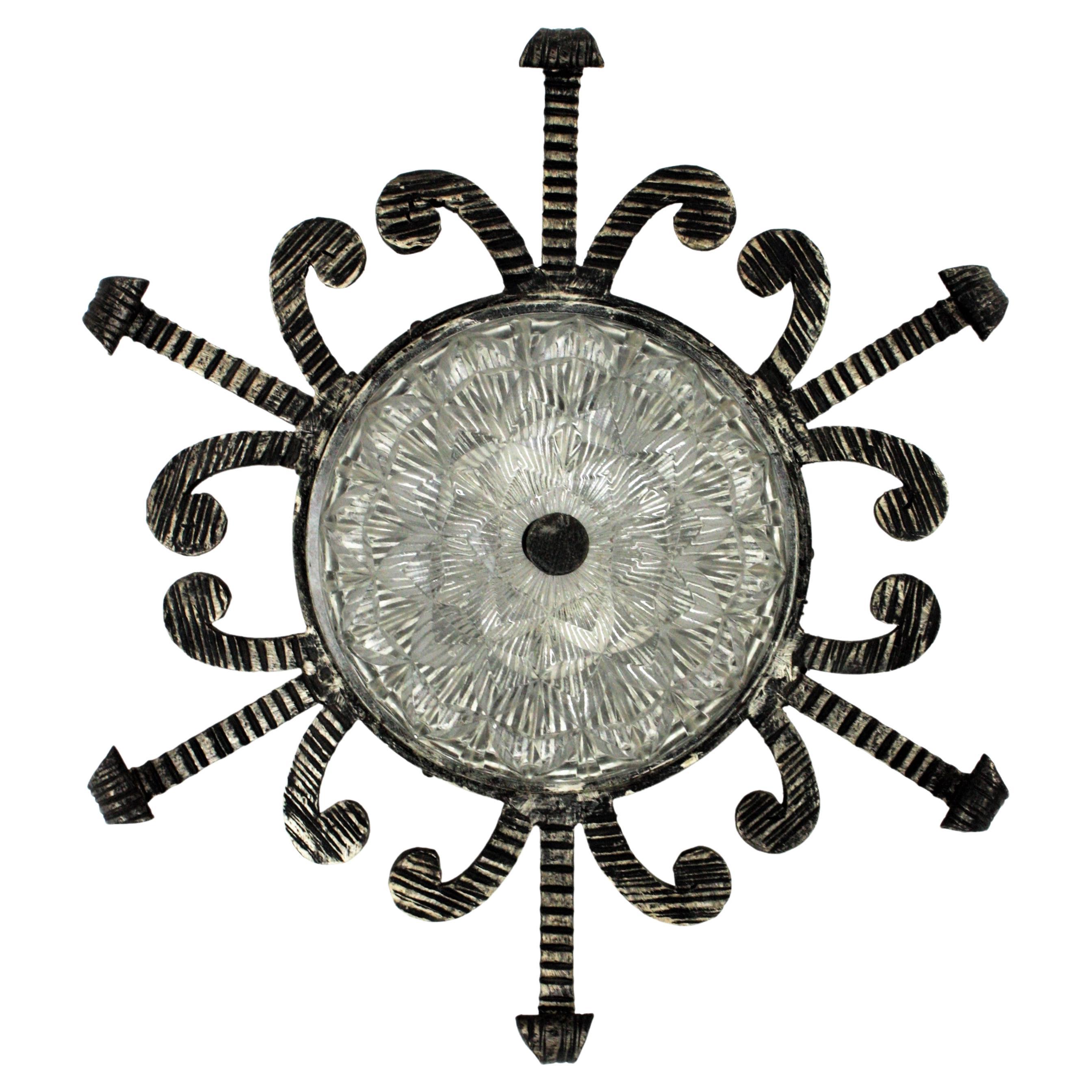 Handsome wrought iron sunburst flush mount / wall sconce with scrolled details and pressed glass shade, Spain, 1950s.
This hand forged light fixture has an interesting design and a very heavy construction. The frame has thick scrollwork accents,