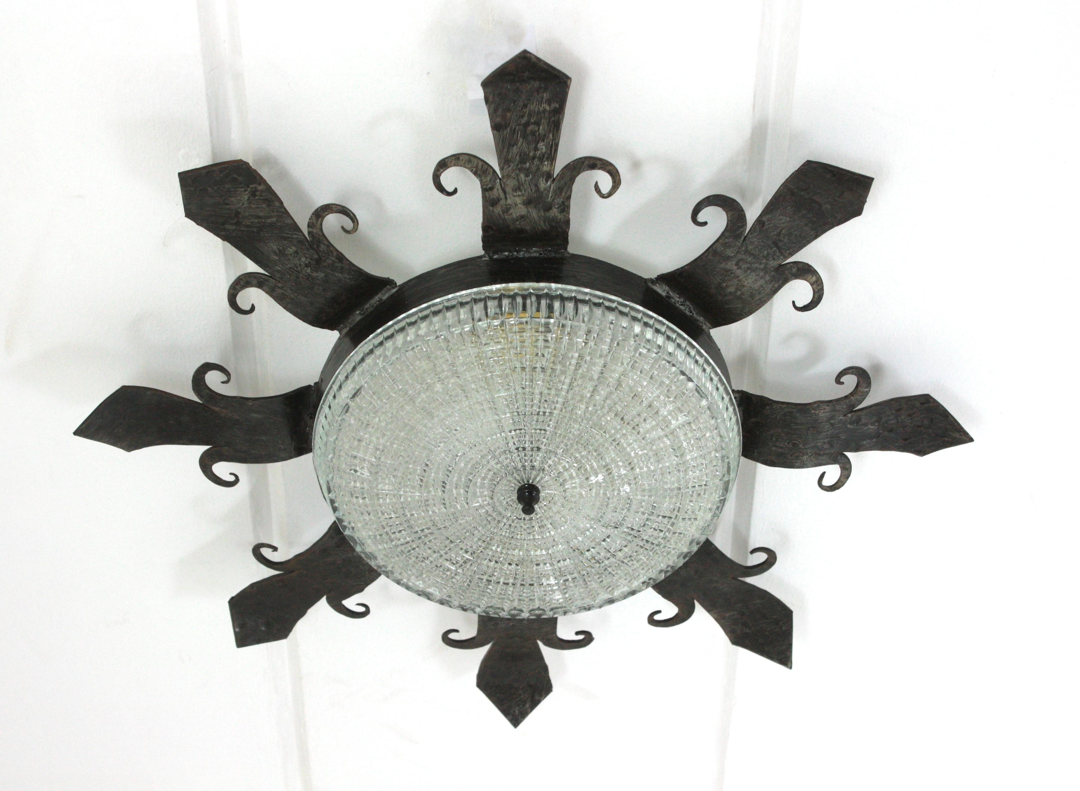 Un luminaire sculptural en fer forgé et en verre aux accents néoclassiques et néo-gothiques. Espagne, années 1940. 
Ce luminaire en fer forgé à la main présente un design très décoratif avec des terminaisons en fleur de lys et des détails de