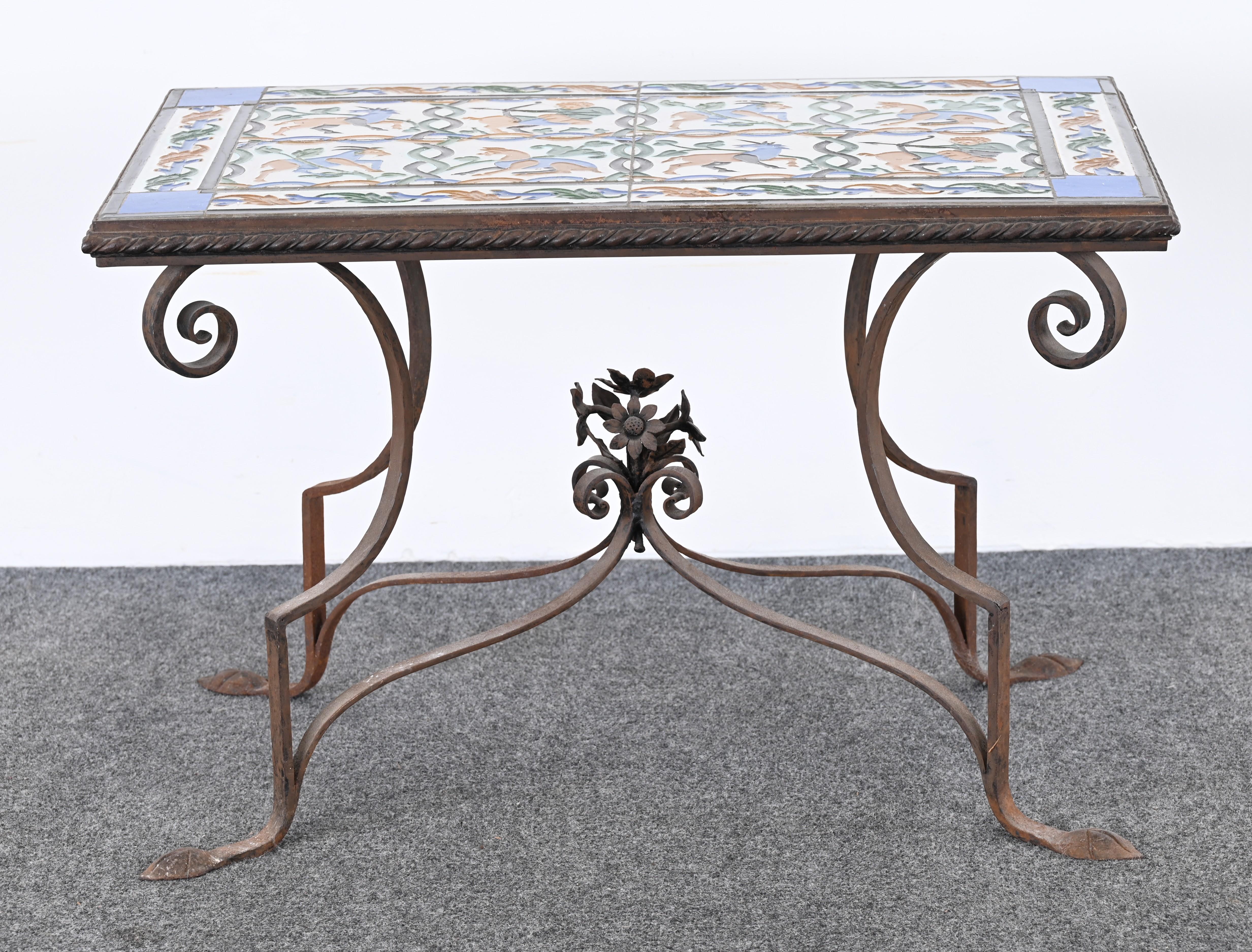 This striking Spanish Revival side table showcases a rectangular top crafted from hand-painted ceramic tiles, featuring a vivid tableau of hunters on horseback pursuing mythical creatures, rendered in rich hues of blue, green, orange, and white. The