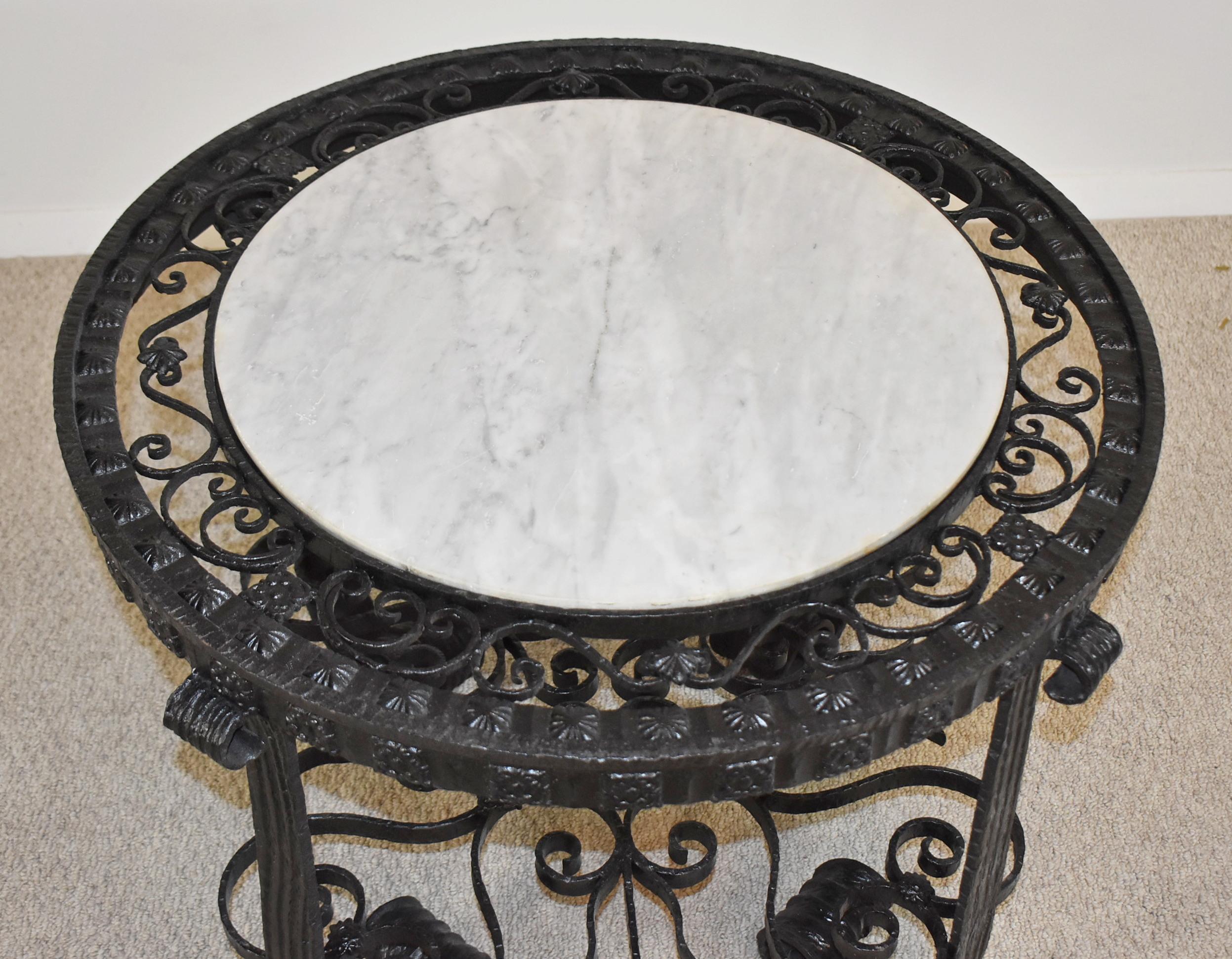 Spanish Revival wrought iron table with marble top. Circa 1920s. Circular inset removable white and gray marble surrounded by iron latticework over four scrolled legs and connected by pierced scrollwork stretcher. South Europe influence in the 20th