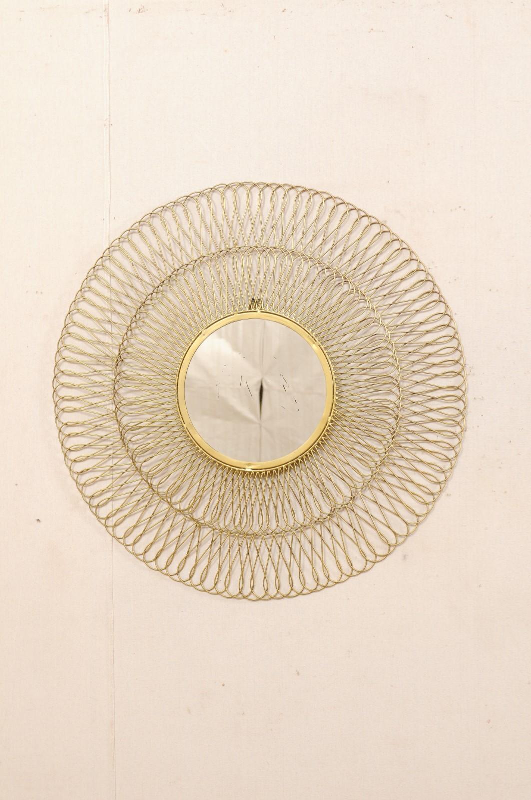 A vintage Spanish round-shaped mirror with brass surround. This decorative wall mirror from Spain features a circular mirror center with a brass surround comprised of two rows of intertwining loops, with an overall diameter of 32 inches. Note that