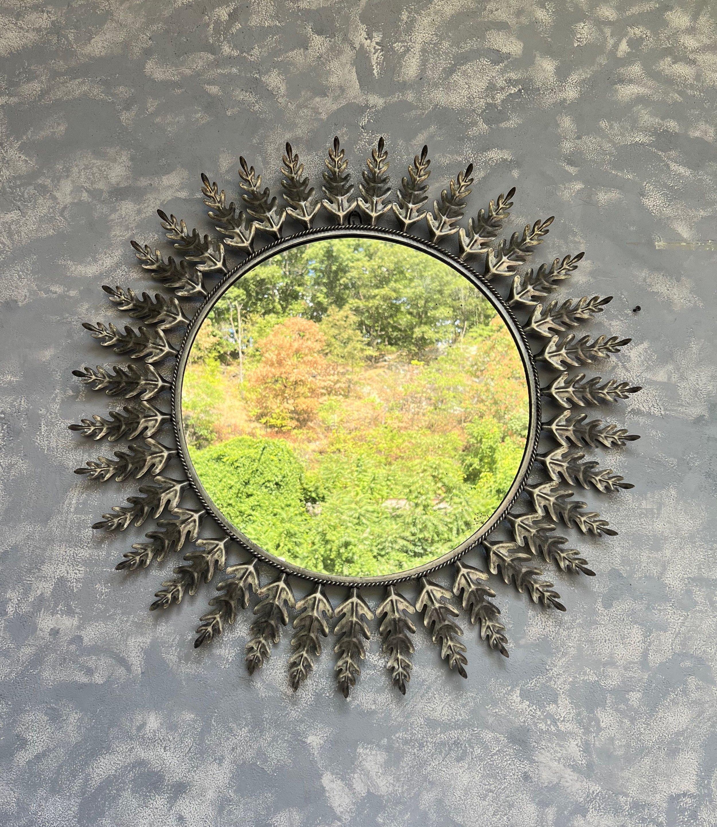 This unique large mid century round sunburst mirror features evenly spaced leaves surrounding a braided interior frame. The metal has a rich, silvered patina. We have added a felt backing to give the mirror more protection and a more finished look,
