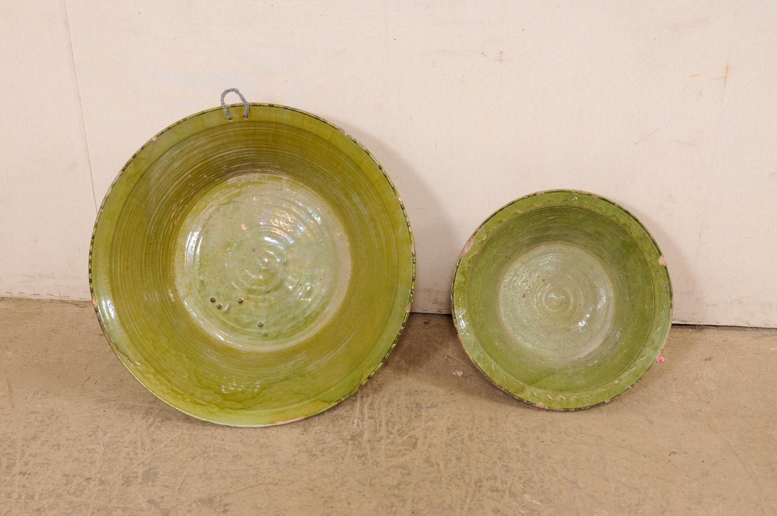 A Spanish pair of glazed terracotta bowl from the early 20th century. These antique bowls from Spain are round in shape, with widest part being at the top lip, and gradually tapering down and resting upon a flat base. There is a green glaze about