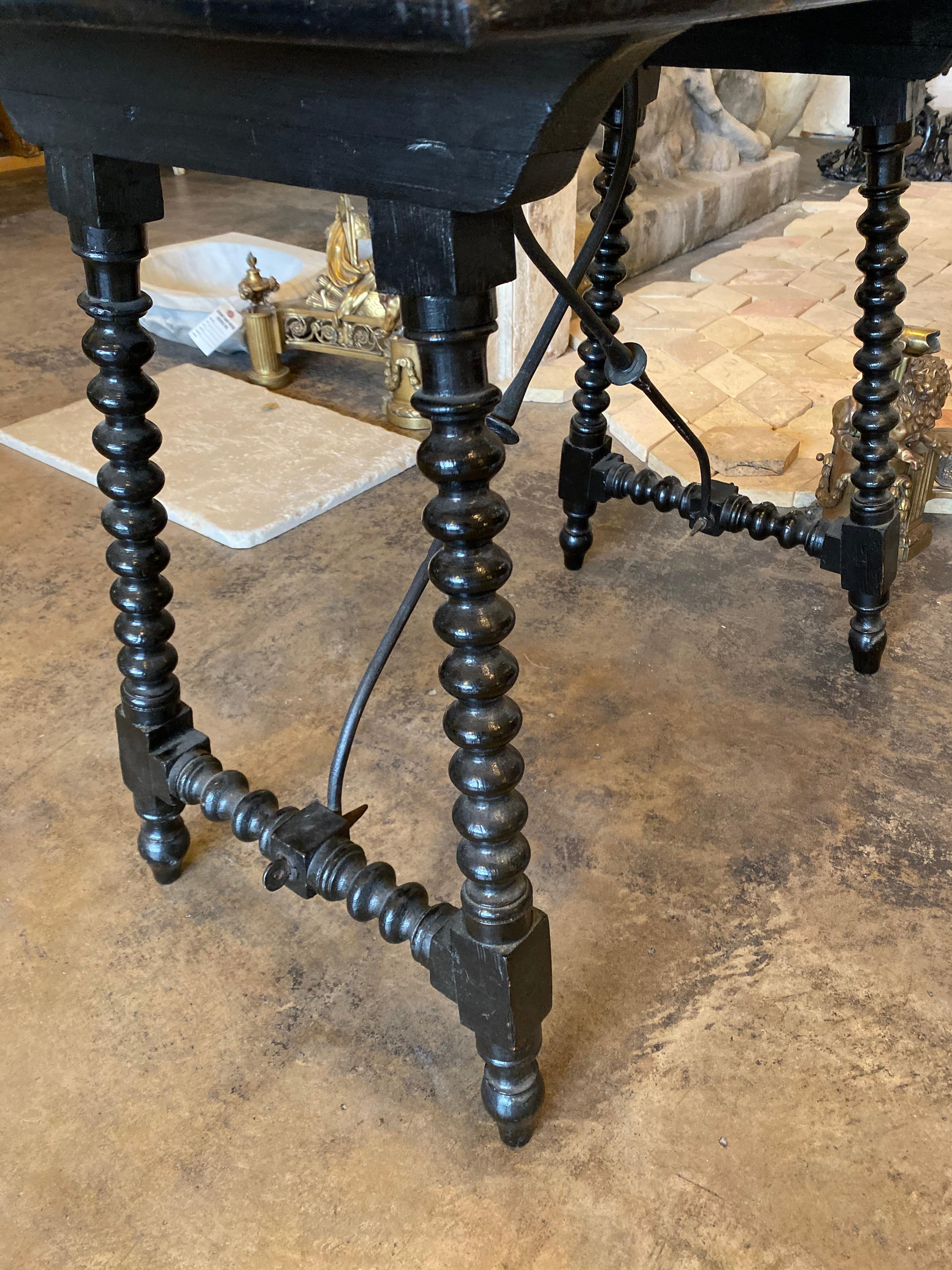 This ebony Spanish side table features signature Spanish detailing with the crisscross base. The top features imagery of a crown, along with country life. An excellent piece for any room.