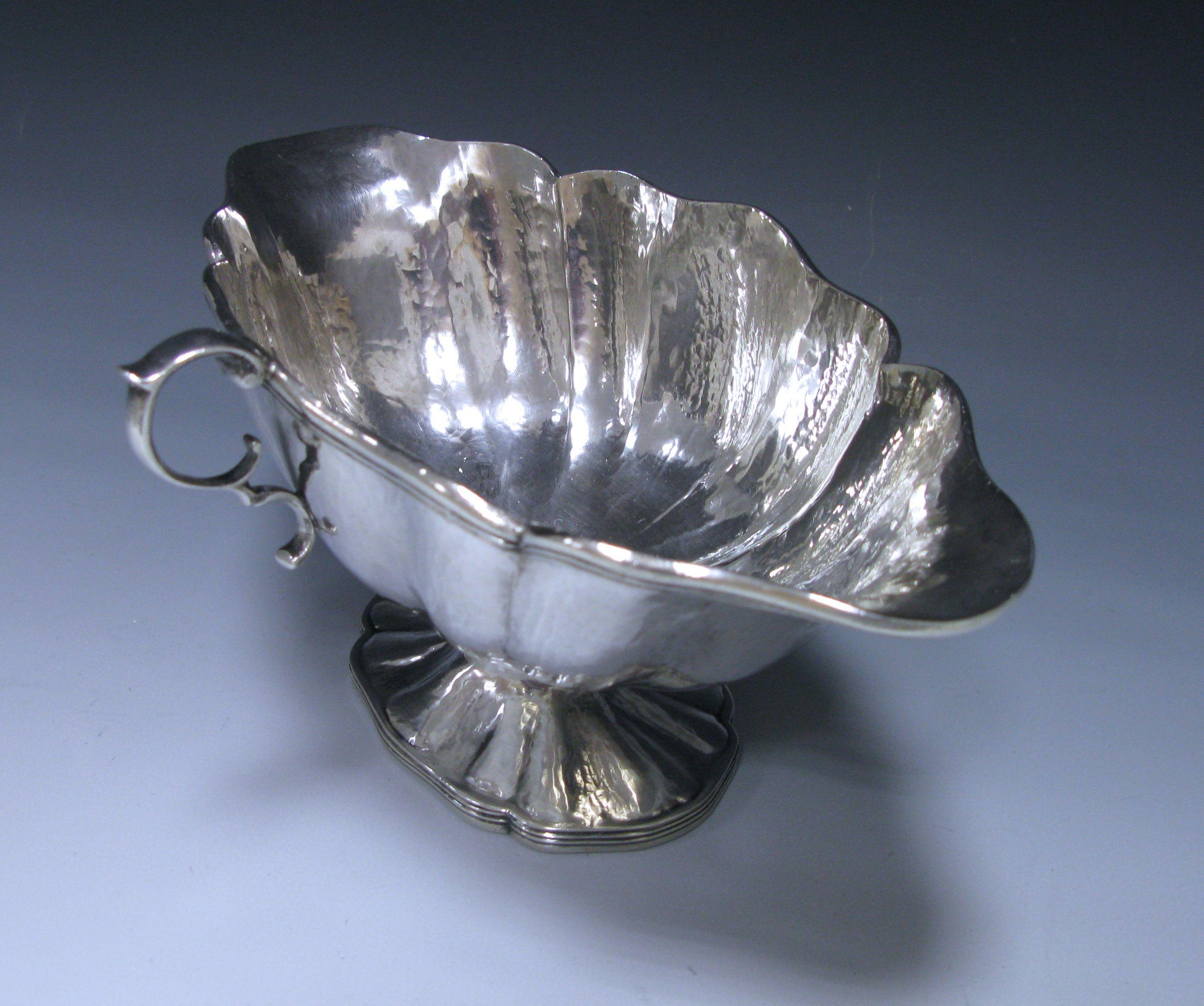 A Spanish sterling 915 standard silver double-lipped sauce boat of shaped oval form with hand-hammered finish. The sauce boat has a single C-scroll handle, an applied reeded rim, all standing on a pedestal foot. Measures: Length 9.25 inches 23.50