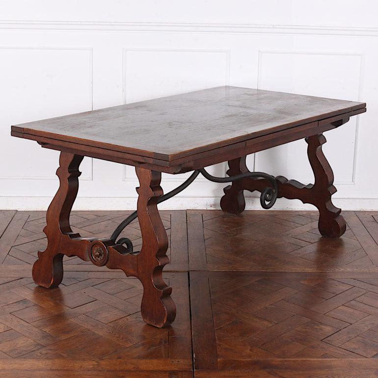 A Spanish style oak trestle table with canted legs and wrought iron scrolled braces. The table has a pull-out leaf at each end and can seat 10-12 people when fully extended. A good sturdy table suitable for everyday use. Nice deep color and