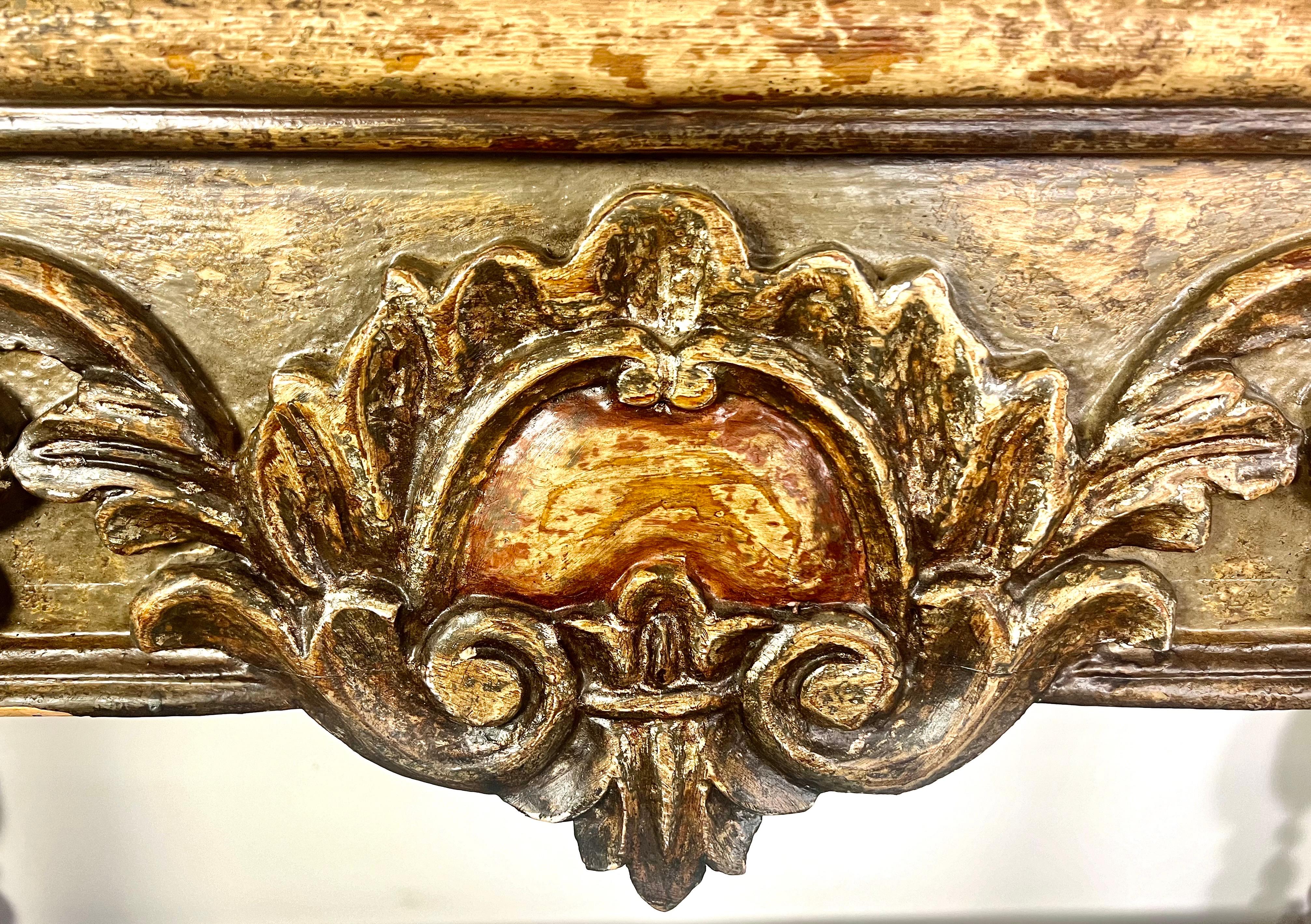 A Spanish colonial style console characterized by its elegant and historic design elements.  At the enter, there is a prominent cartouche adorned with a carved center medallion, surrounded by detailed acanthus leaves, showcasing the intricate