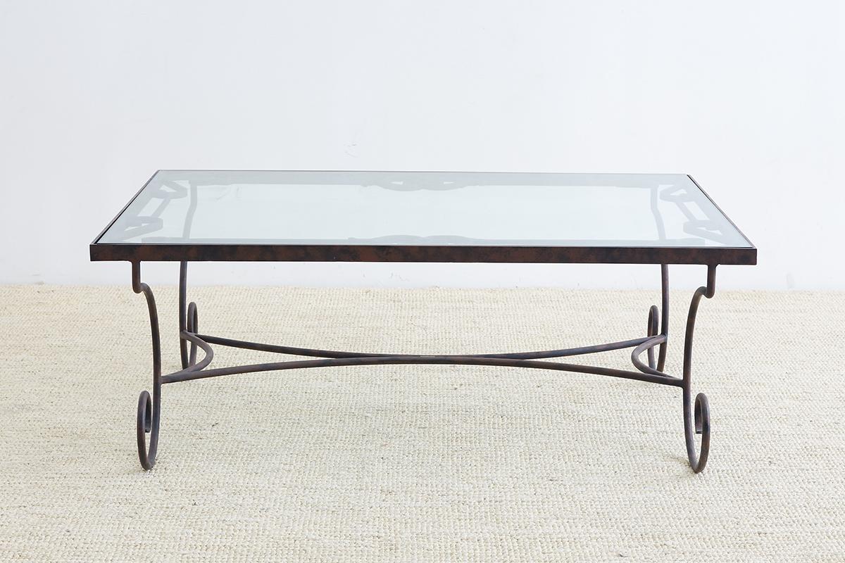Elegant Spanish style coffee or cocktail table made from wrought iron. Features a thick rectangular top decorated with scrolled designs around the border and topped with a thick pane of glass that fits flush. Supported by dramatic scrolled legs