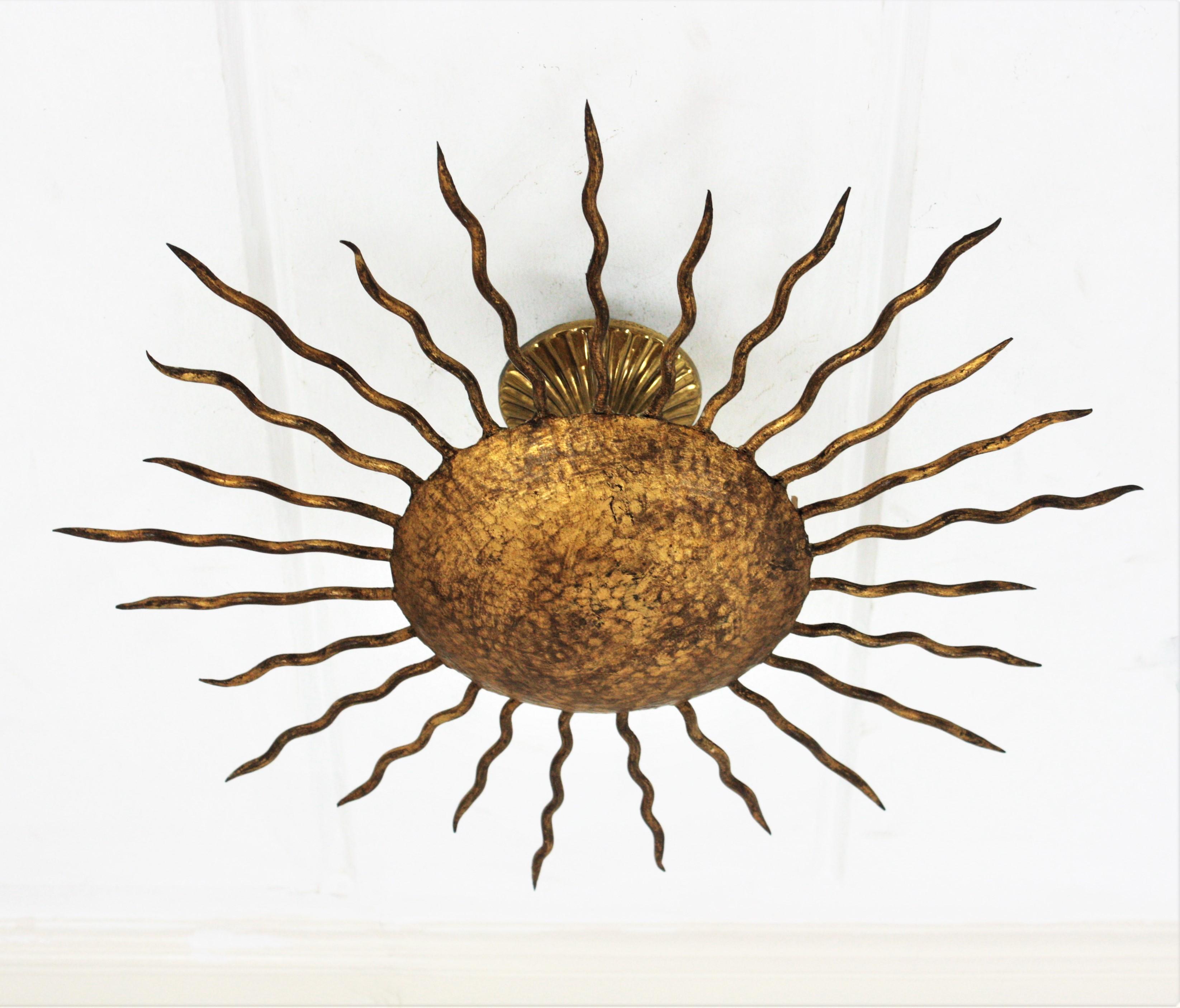 Gold leaf gilt wrought iron sunburst flush mount, Spain, 1950s.
Hand-hammered sunburst light fixture richly decorated in the central part by the hammer marks. Curly iron rays surrounding the central sphere.
Original gold leaf gilding and nice