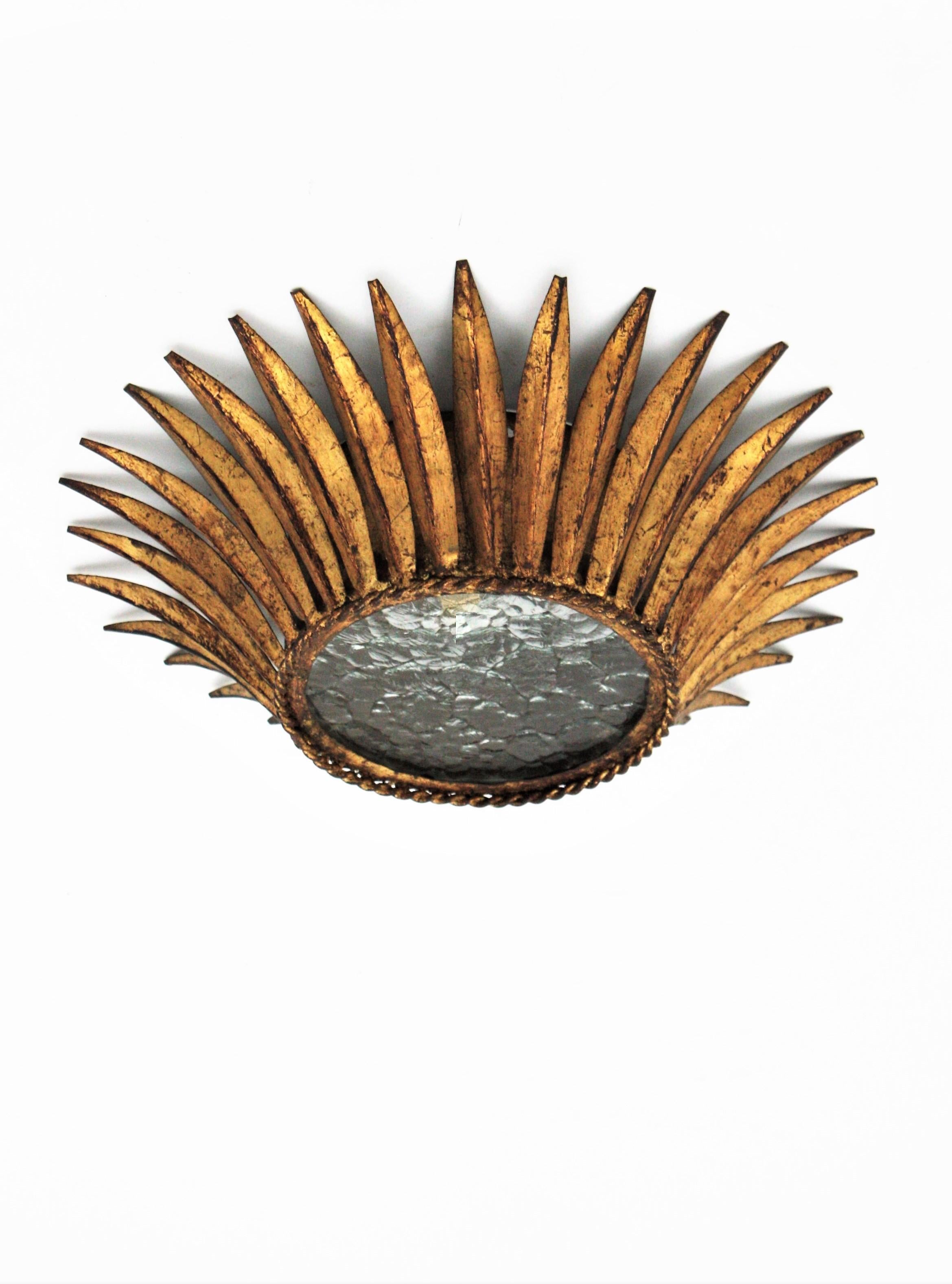 Montatura da incasso a forma di corona forgiata a mano, ferro dorato, vetro testurizzato, Spagna, anni '50.
Un'elegante lampada a raggiera a forma di corona o a incasso in ron dorato con diffusore in vetro trasparente testurizzato. Ha una sola