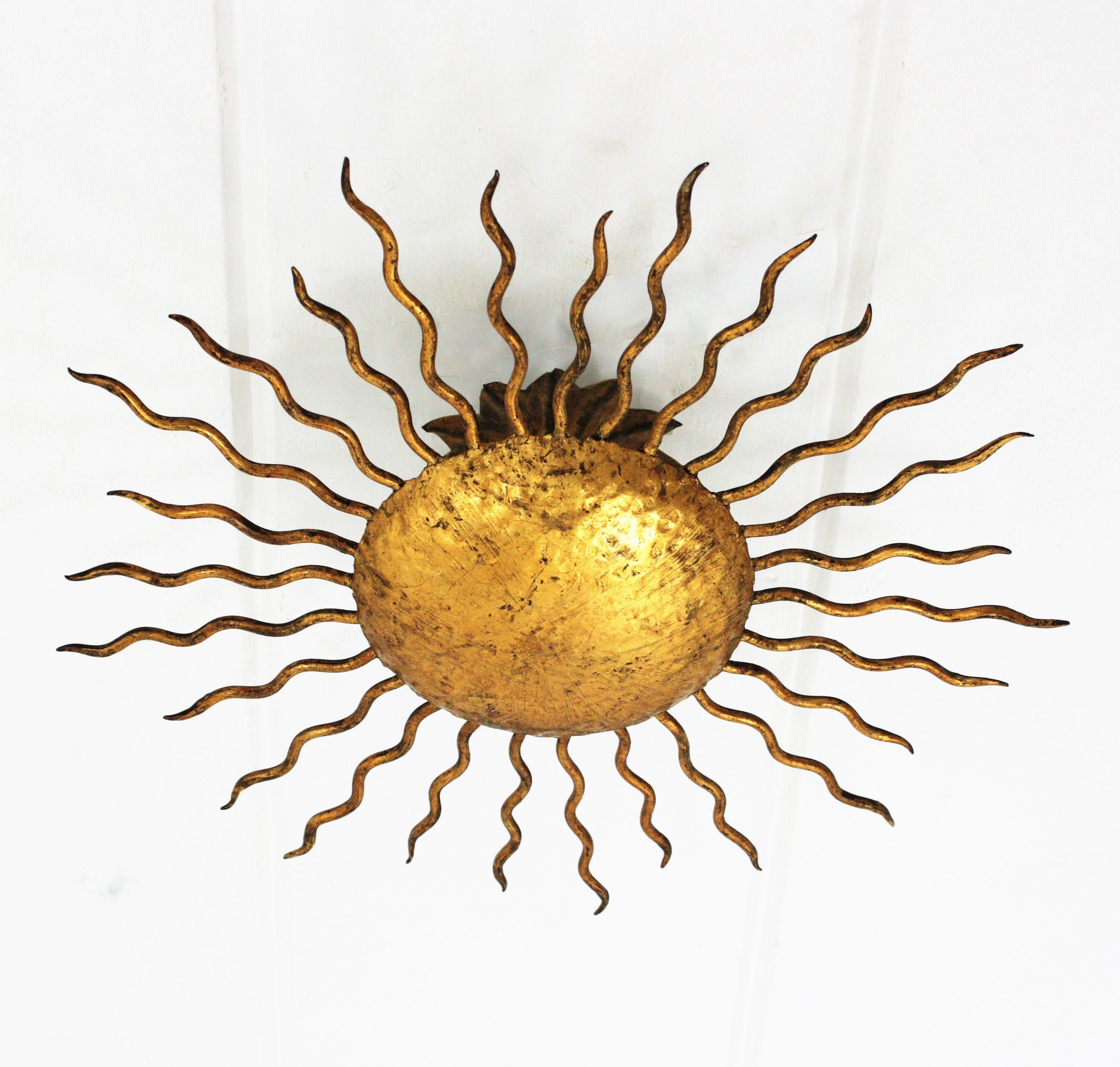 Gold leaf gilt wrought iron sunburst light fixture, Spain, 1950s.
Richly decorated in the central part with hand-hammered marks. Curly iron rays surrounding the central sphere.
Beautiful to place as ceiling light fixture but also as a wall sconce.