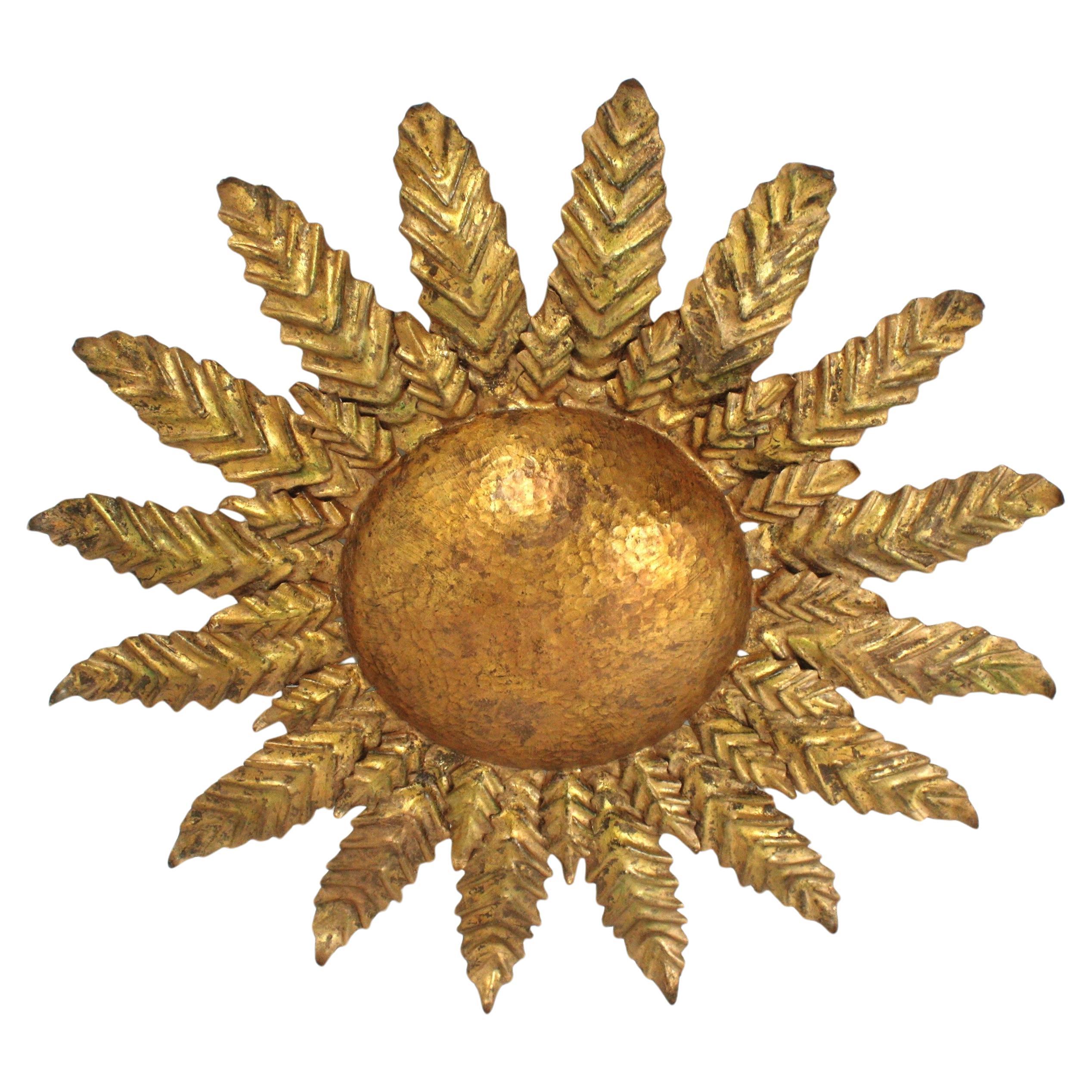 Auffällige Deckenleuchte aus vergoldetem Schmiedeeisen mit Sonnenschliff-Blättern. Spanien, 1950er Jahre.
Dieses Stück zeigt eine Deckenleuchte mit Sonnenschliff und Blumen, die reichlich handgehämmert ist. 
Es zeigt eine exquisite Schmiedearbeit