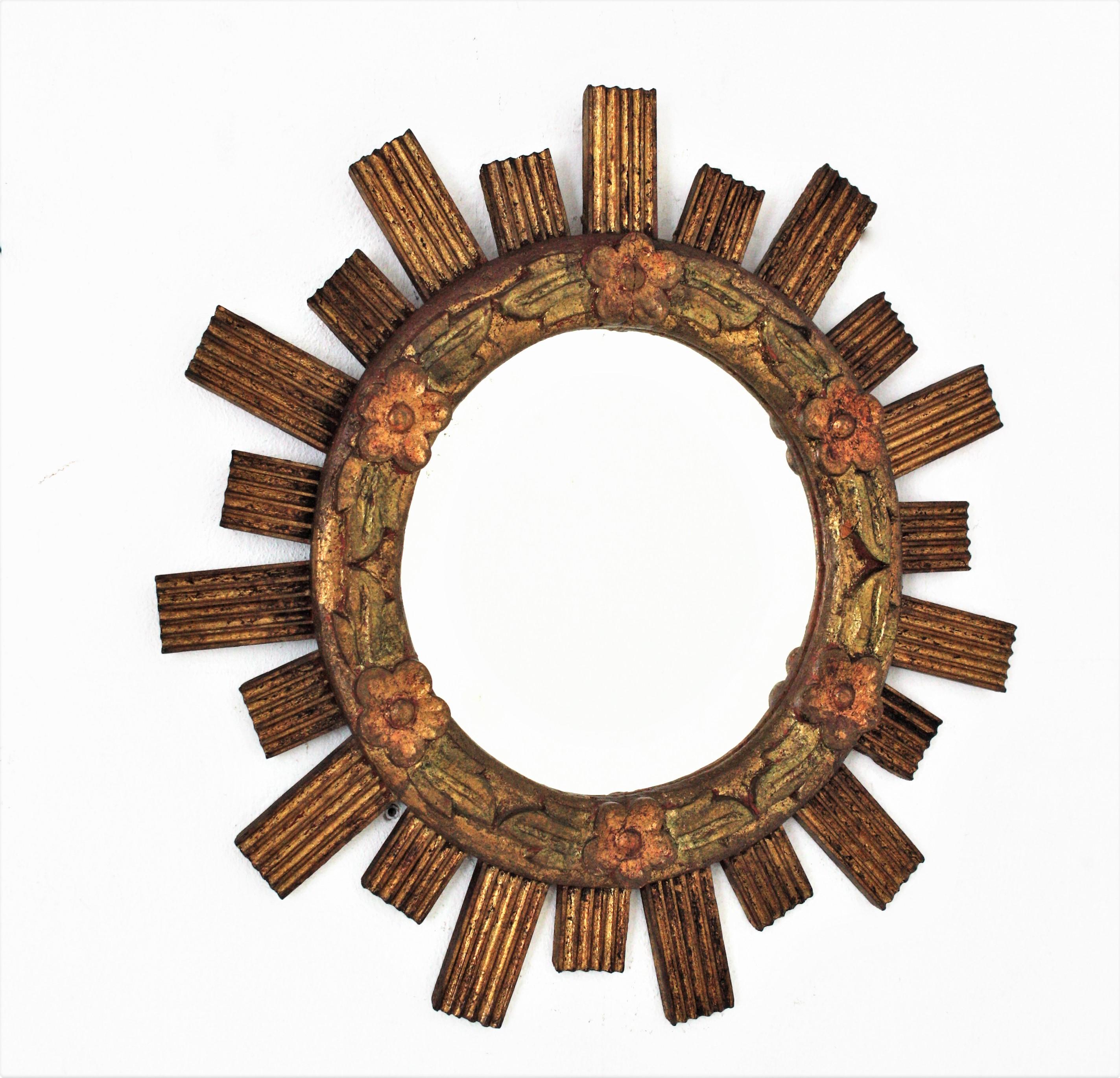 Outstanding carved and gilded wood round sunburst mirror with floral foliage frame. Spain, 1960s.
Carved wood and gold leaf gilding. The frame has striped carving details on the rays and small polychrome carved flowers adorning the central part. It