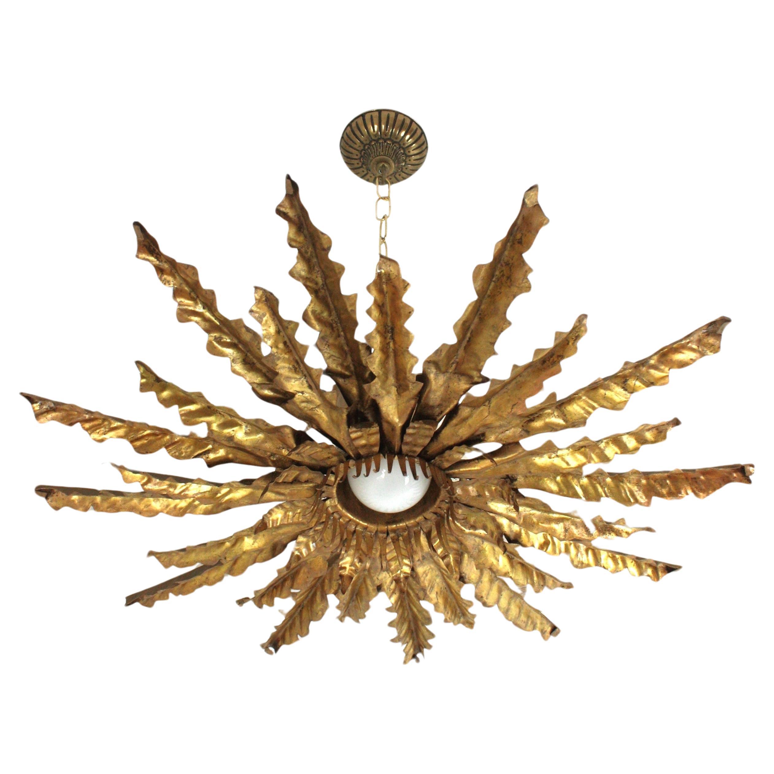 Monumental brutalist sunburst foliage gilt metal ceiling light fixture. Spain, 1950s
This handcrafted Brutalist ceiling lamp features a triple layered leafed sunburst light fixture.The handcut and hand-hammered iron leaves have a detailed work and