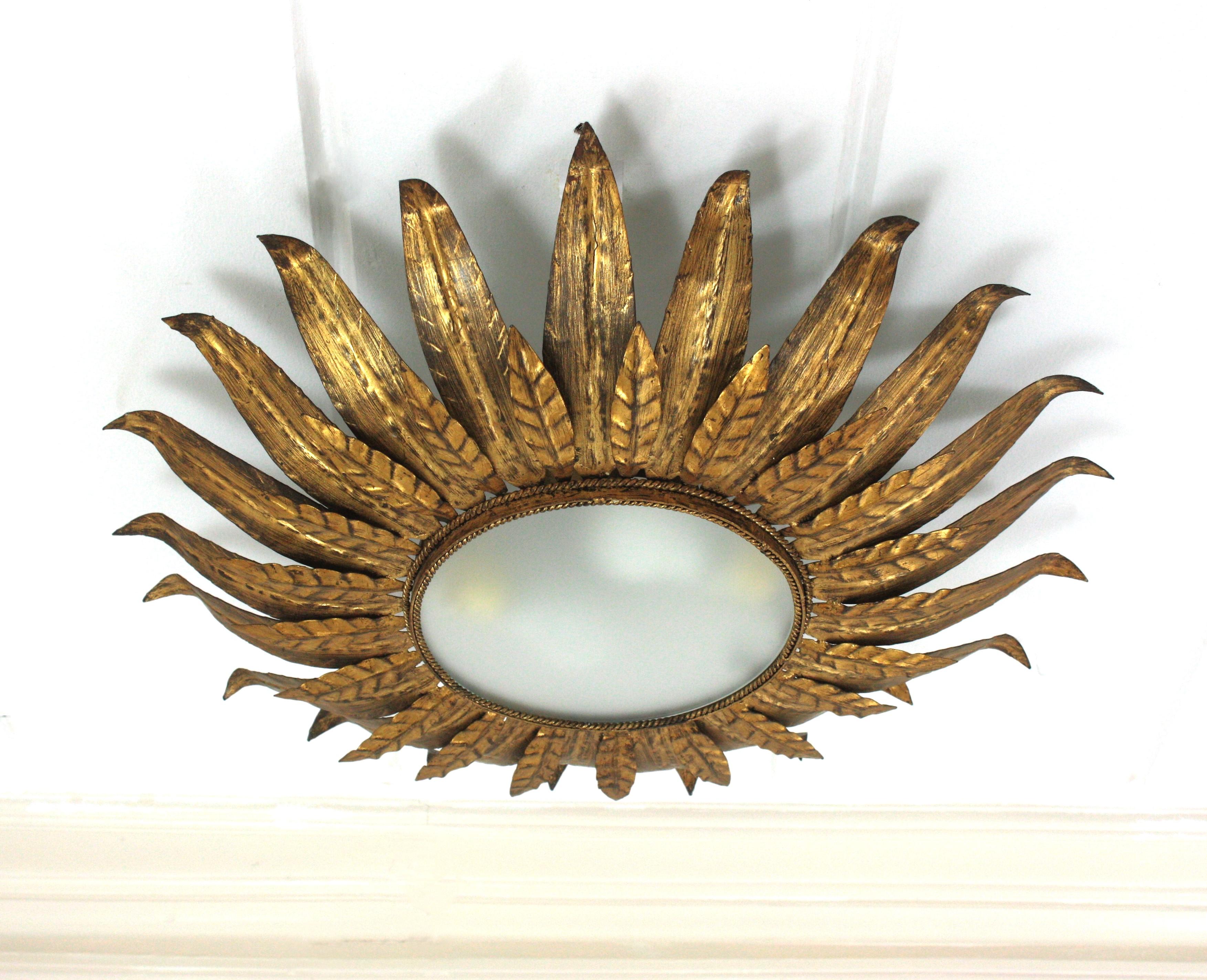 Large Sunburst Foliage Flower Light Fixture, Gilt Metal, Frosted Glass

Mid-Century Modern gilt iron sunburst flush mount or pendant with leaf motifs surrounding a central frosted glass diffuser, Spain, 1950s.
Double layer of gilt iron leaves frame.