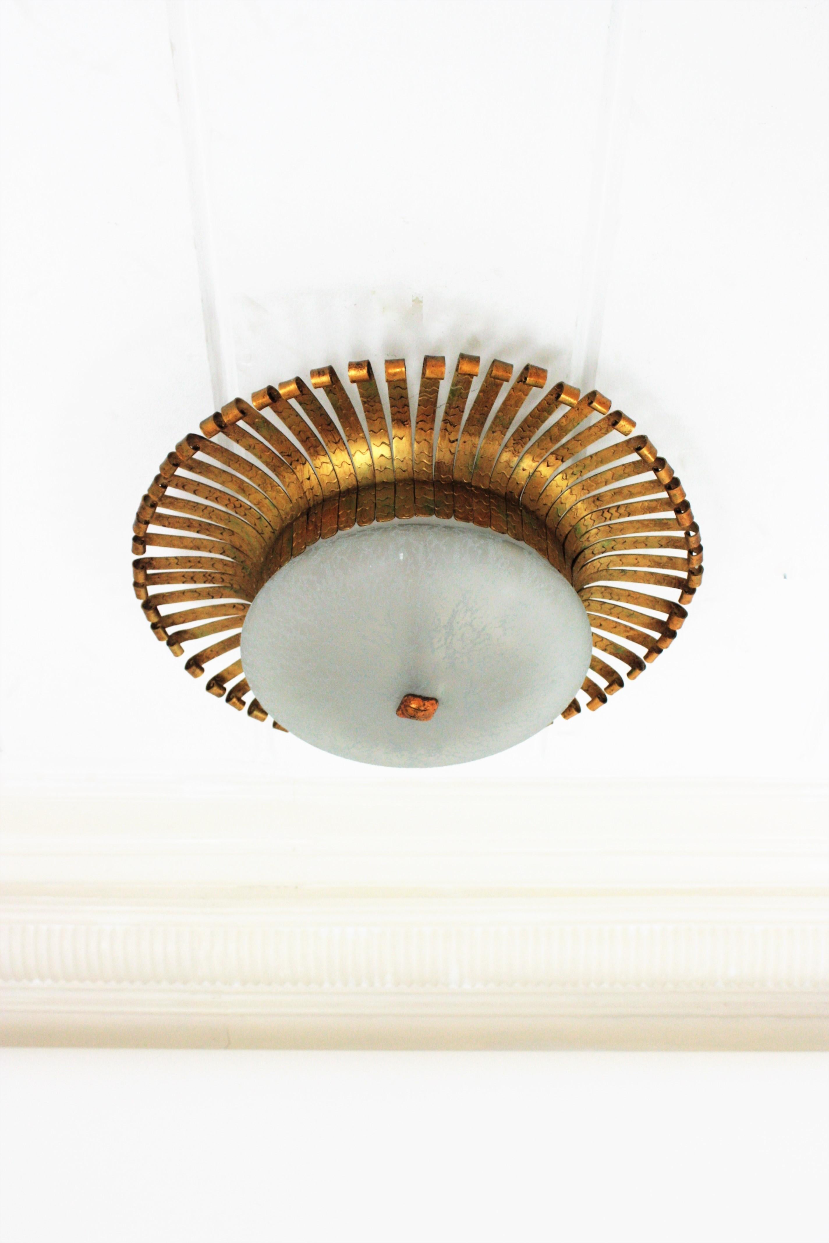 Eyelash sunburst light fixture in gilt iron and glass, Spain, 1950s-1960s.
This flush mount or wall light features a sunburst iron backplate surrounding a central frosted glass globe lampshade.
Handcrafted in hammered iron with gold leaf