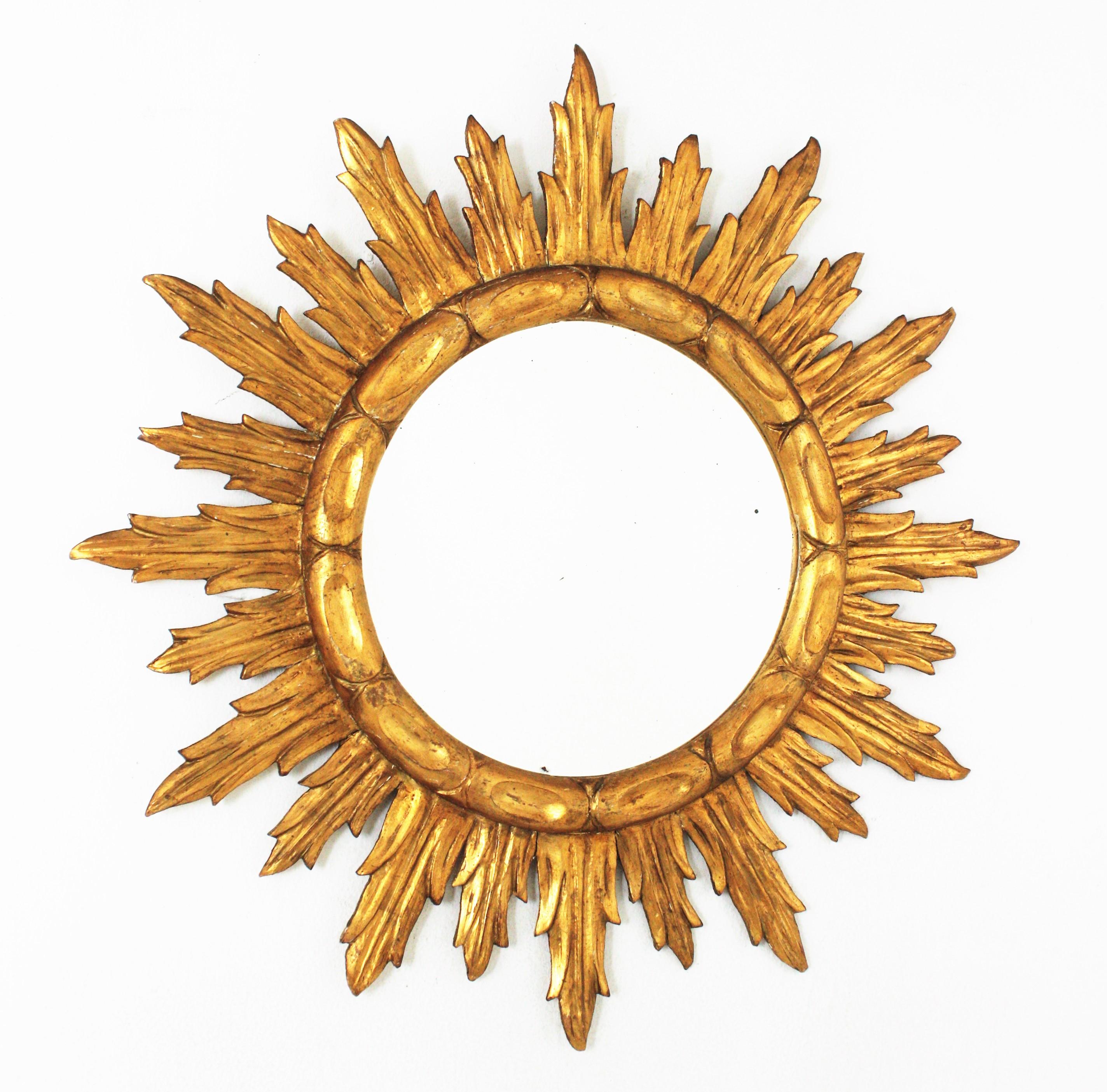 Outstanding finely carved and gilded wood sunburst mirror. Spain, 1940s-1950s
Carved wood and gold leaf gilding. The frame has finely carved rays in two sizes and a patterned round ring surrounding the central glass. It has a nice patina showing