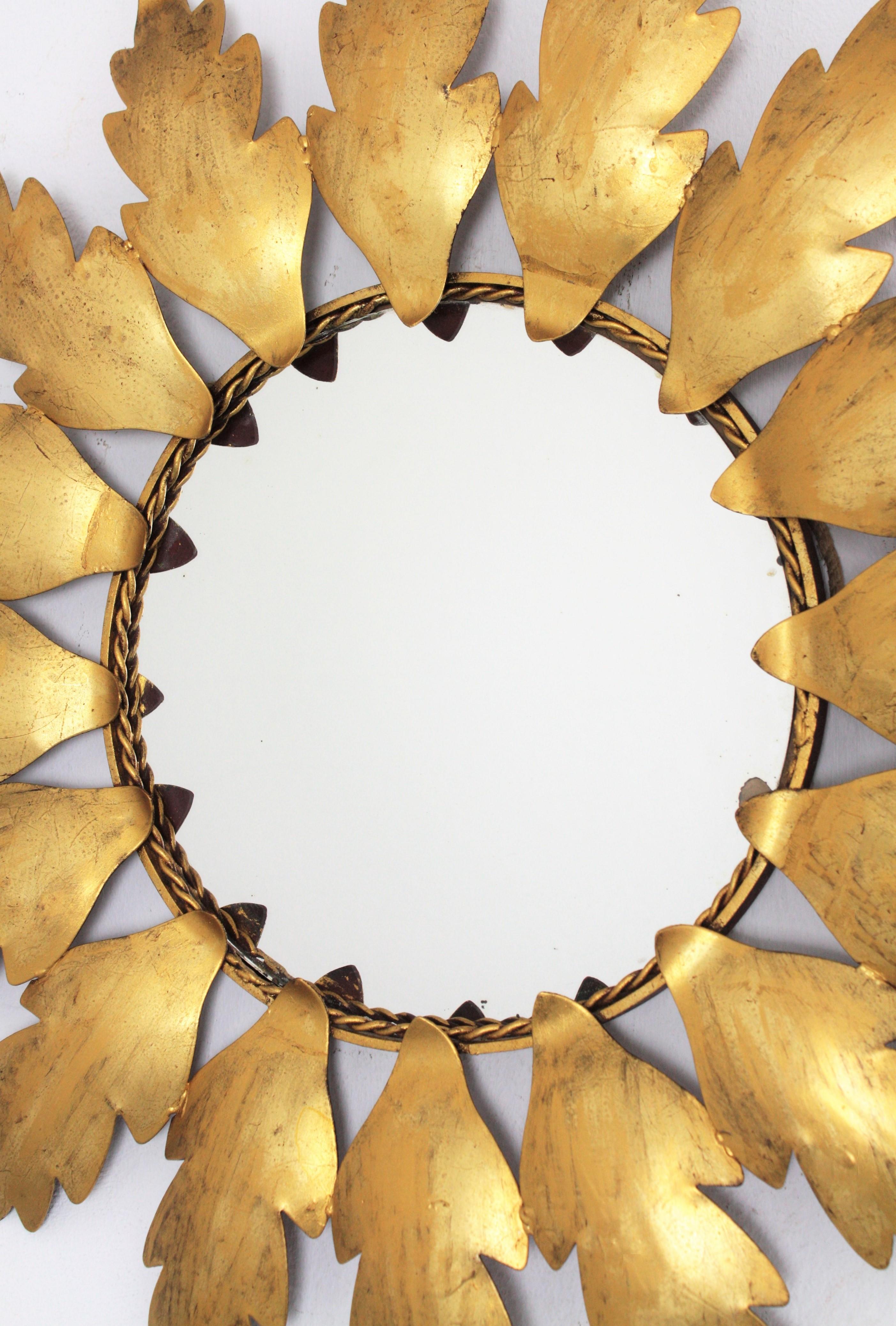 Beautiful handcrafted gilt iron flower shaped leafed sunburst mirror, Spain, 1960s.
It has leaves surrounding a central round glass in sunburst or flower shape disposition. 
Measures: Overall diameter: 50 cm // Diameter of the glass: 22 cm.

   