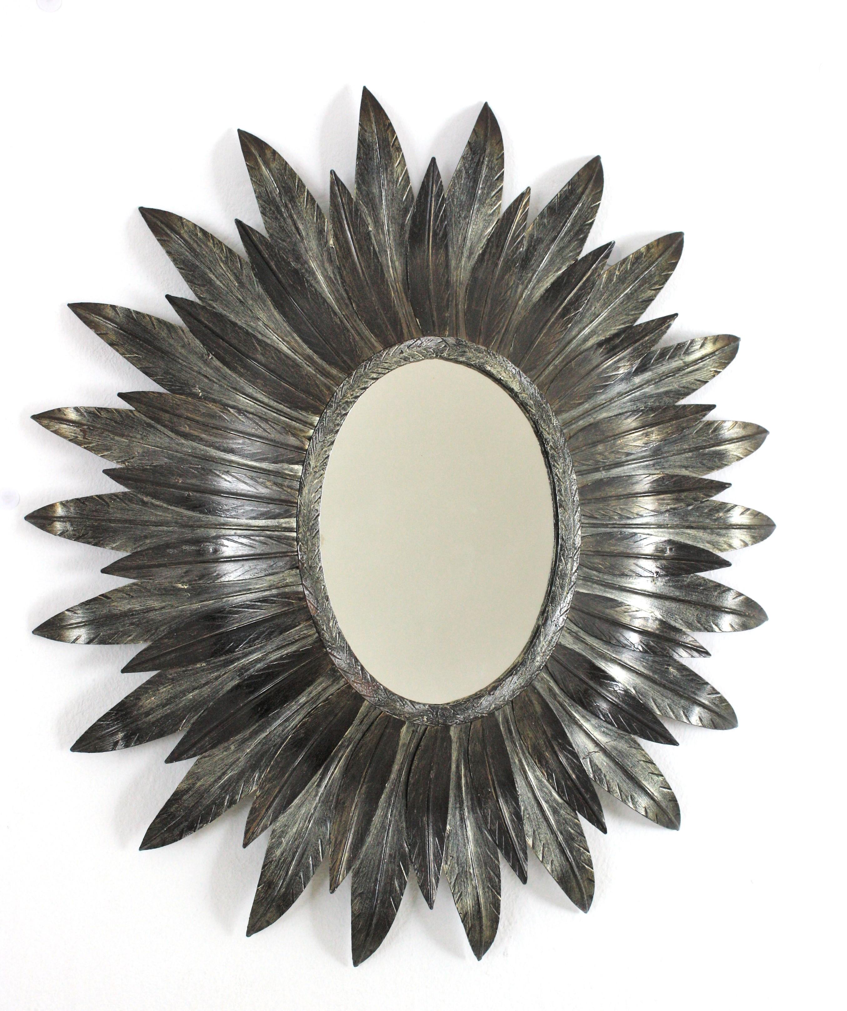 Auffälliger ovaler Sunburst-Spiegel aus versilbertem, vergoldetem Metall Spanien, 1950-1960.
Dieser Wandspiegel mit Sonnenschliff verfügt über ein ovales Glas, das von geschwungenen versilberten Metallblättern in zwei Größen eingerahmt