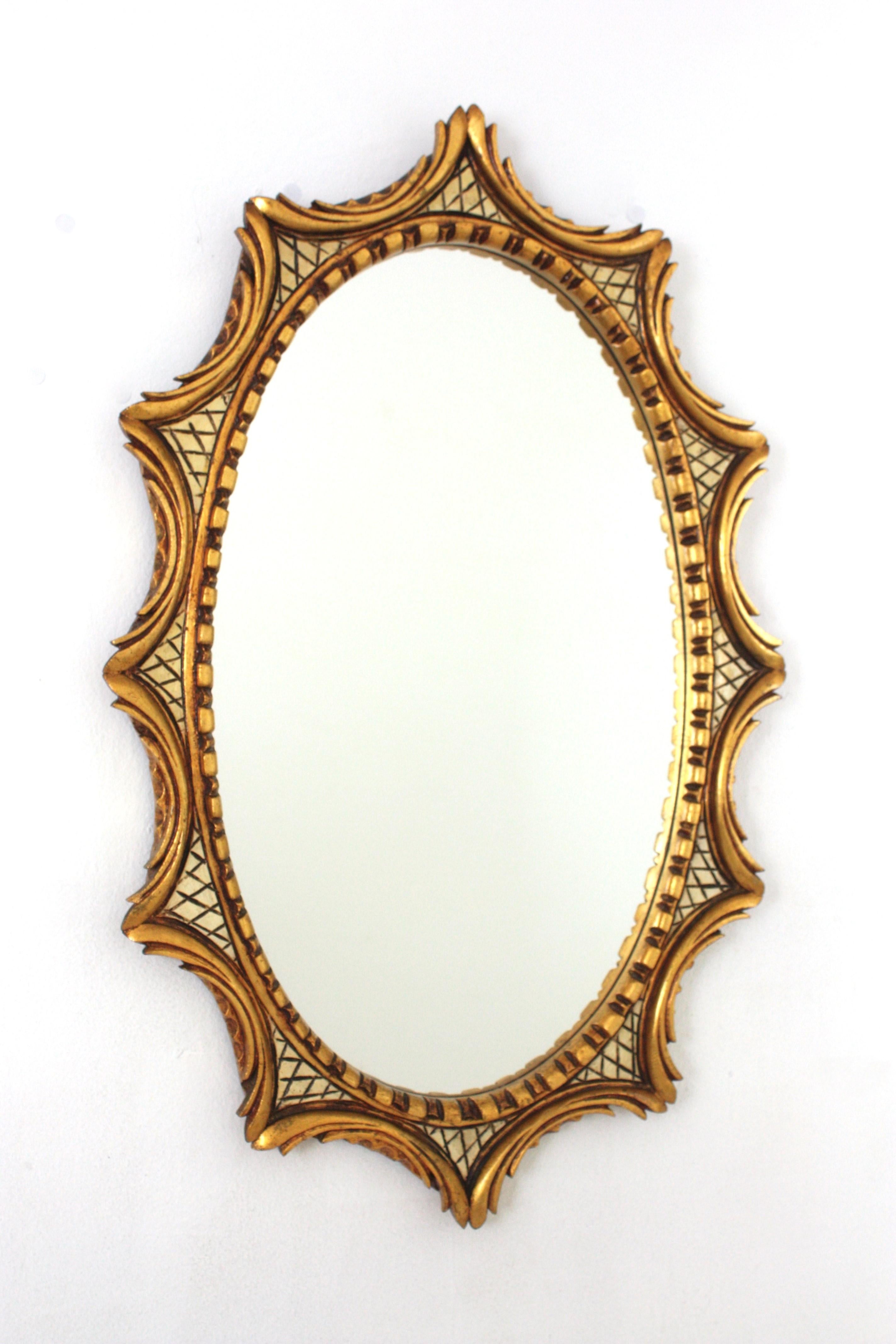 Hollywood Regency Giltwood Oval Sunburst Mirror, Spain, 1950s-1960s.
One of a kind gilt oval wall mirror framed in starburst or sunburst shape. Nicely carved foliage inspired scroll details with an scalloped pattern surrounding the glass. The frame