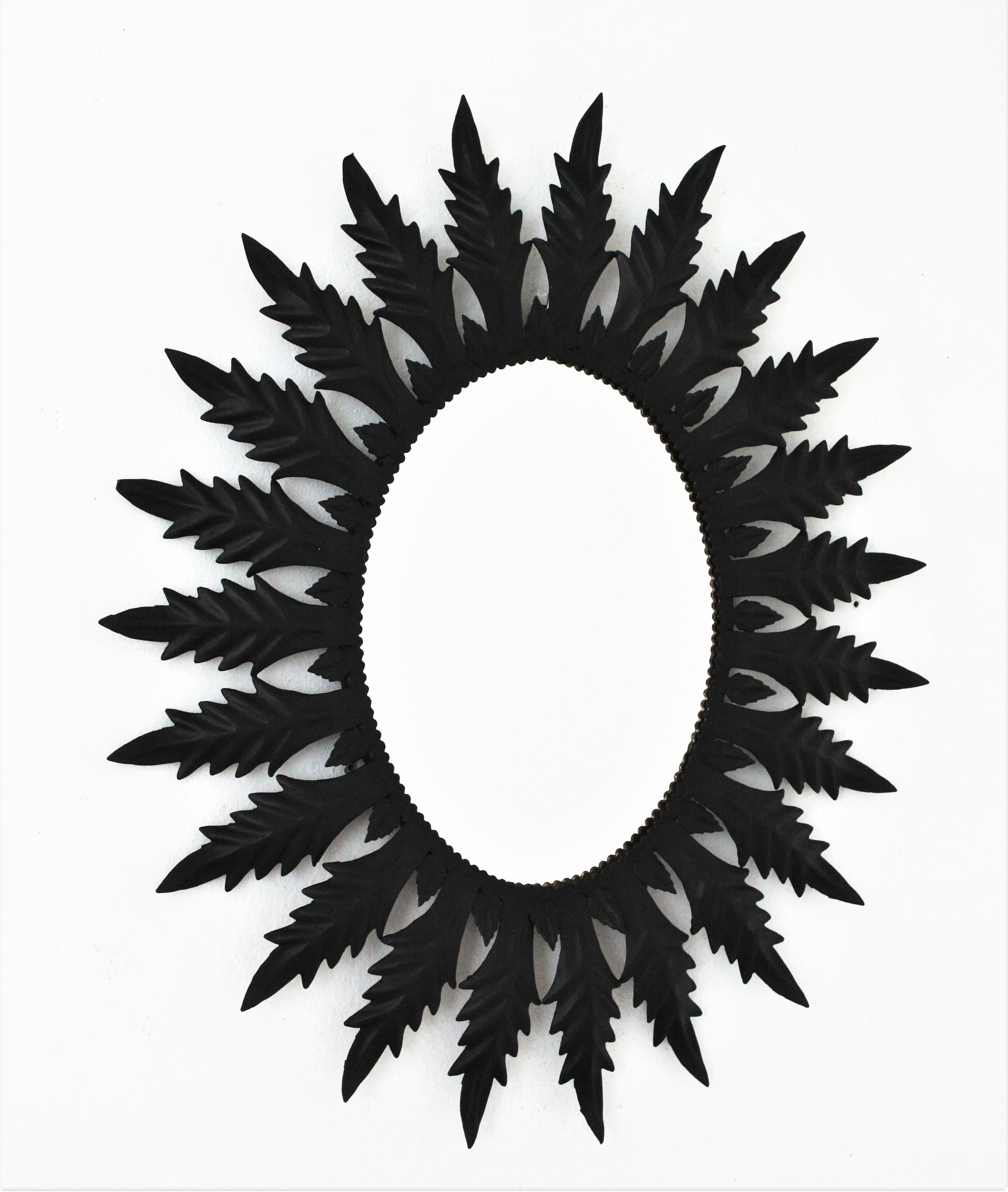 An eye-catching oval sunburst mirror handcrafted in metal with black painted finishing, Spain, 1960s.
The frame of this oval mirror has a layer or large leaves and a layer of small leaves surrounding the glass. 
This wall mirror would be a nice