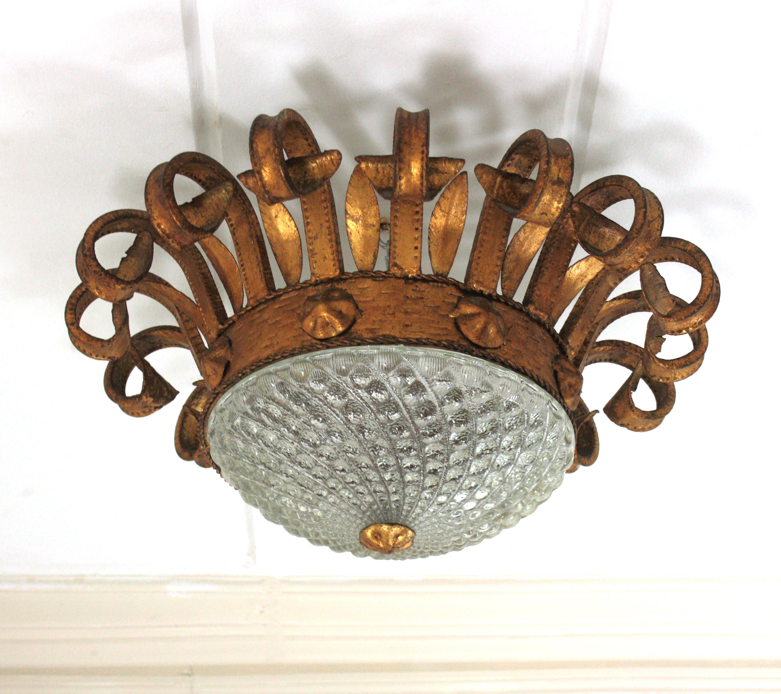 Lampe à couronne unique en son genre, en fer forgé, feuille d'or, verre pressé, 
Espagne, années 1940
Grande taille.
Ce superbe plafonnier se compose d'un cadre en fer forgé à la main en forme de soleil, avec des extrémités en forme de cils et de
