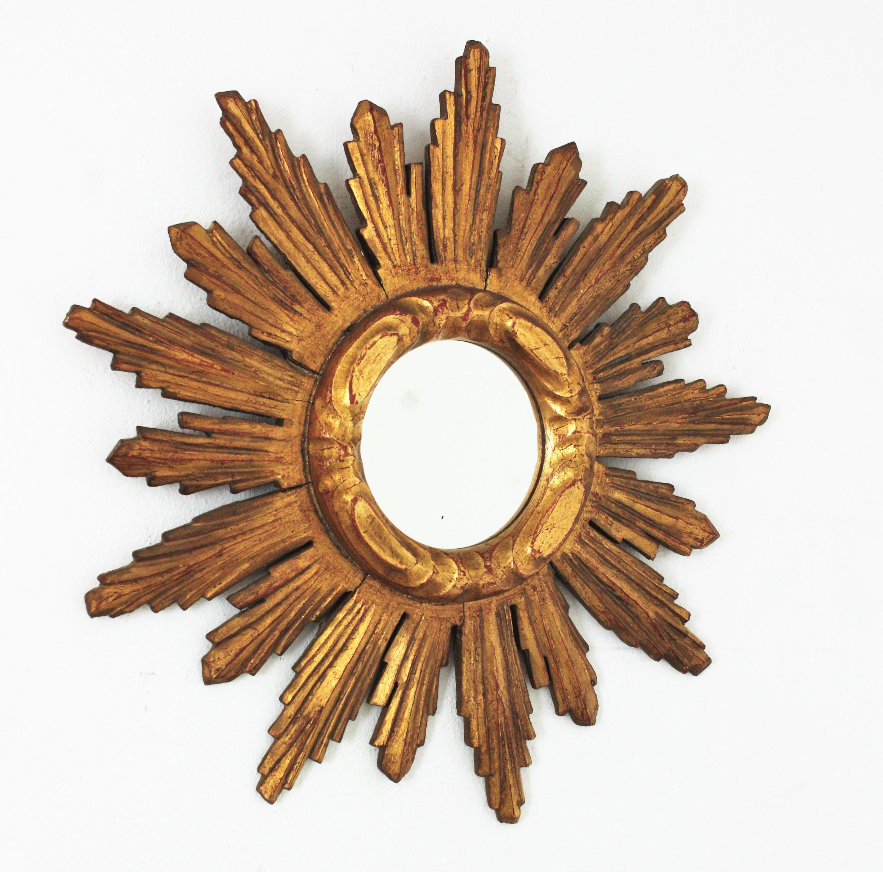 Baroque style carved giltwood sunburst mirror. Spain, 1950s
Eye-catching giltwood sunburst mirror with carved frame and patterned ring surrounding the central round glass
This wall mirror has richly carved details and gold leaf gilding and It has