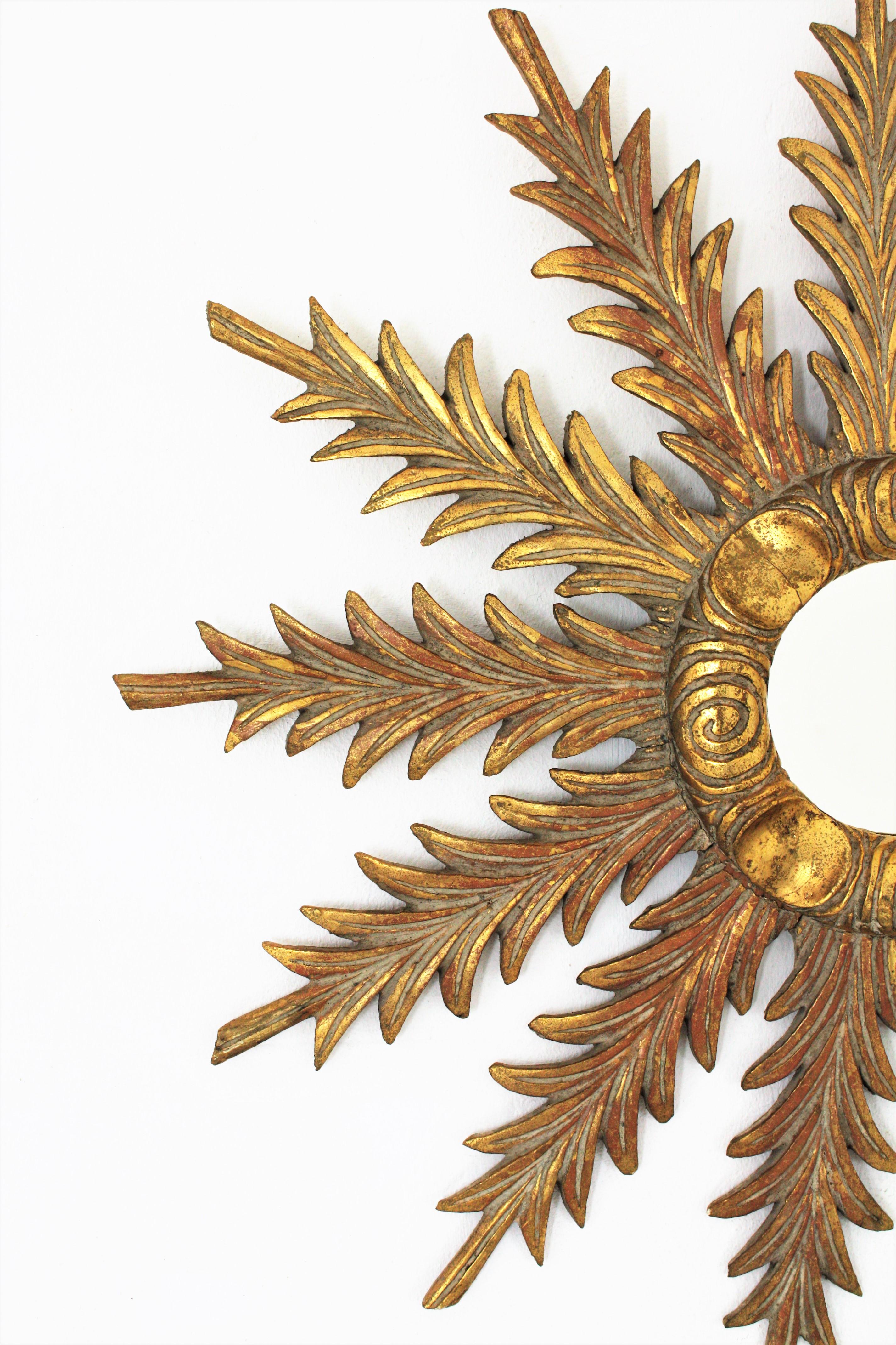 Starburst sunburst mirorr, carved wood, gold leaf,  Spain, 1930s
Elegant leafed starburst sunburst mirror combining Hollywood Regency and Baroque Style accents. The frame is richly adorned by finely carved leaves surrounding a central round mirror