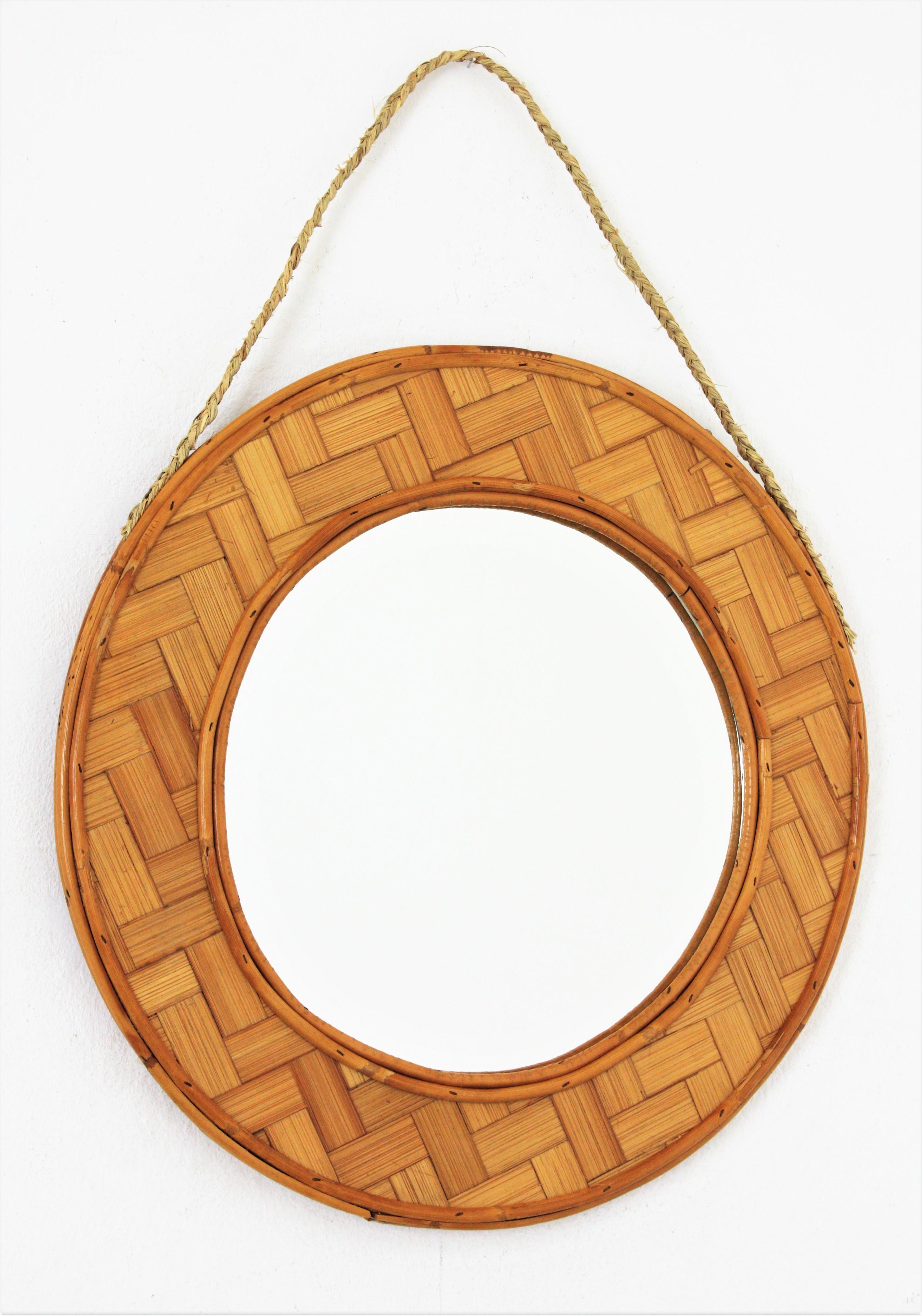 Spanish Tiki Style Woven Bamboo and Rattan Hanging Mirror, 1960s
Mid-Century Modern handcrafted braided bamboo leaf and rattan circular mirror hanging from an esparto rope. 
This lovely circular hanging mirror features a frame with an intrincate of