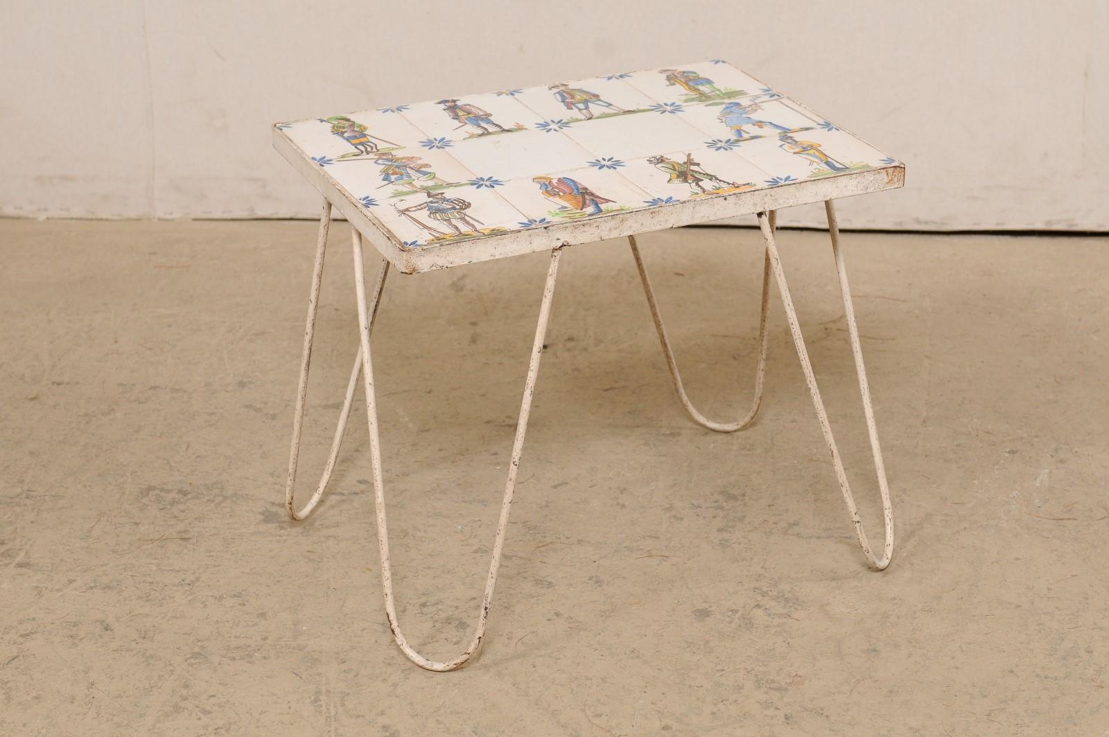 A Spanish decorative tile top side table on metal base. This vintage side table from Spain has been adorn with a series of artisan painted tiles portraying various military figures, set around the perimeter with center being simple white tiles (but