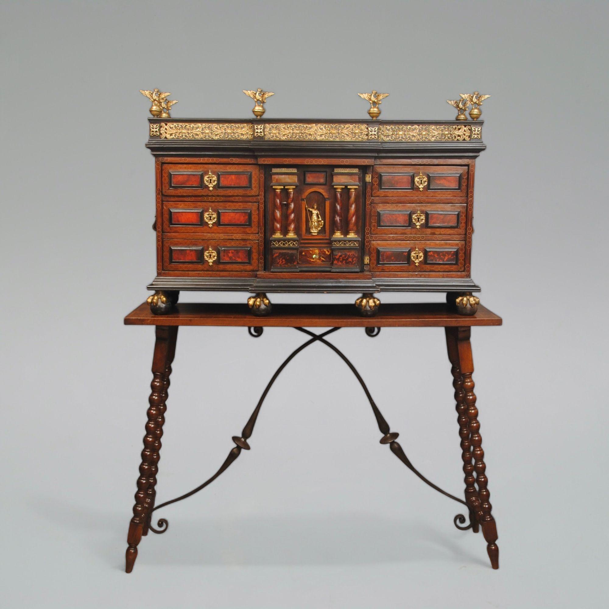 Un mueble español montado en ormolu sobre soportes originales. Los bancos de cajones a ambos lados de un armario central, todos con paneles de concha de tortuga roja y columnas torneadas. De pie sobre patas de garra.
El soporte de la mesa de abajo