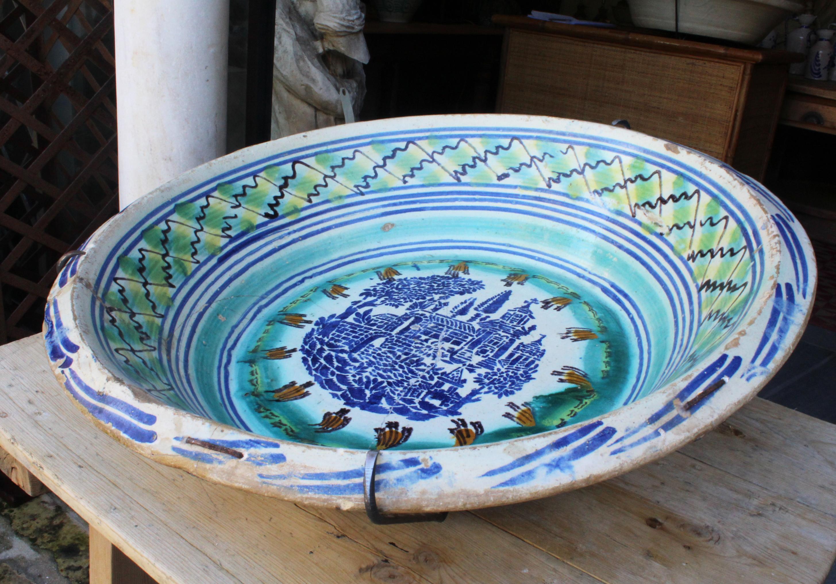 19th century Spanish Triana whit green, blue and yellow glazed terracotta plate.

Triana is a style that originates in Seville, known for its mix of Christian and Al-Andalus cultures.

With escenes of a town and trees in the middle and geometric