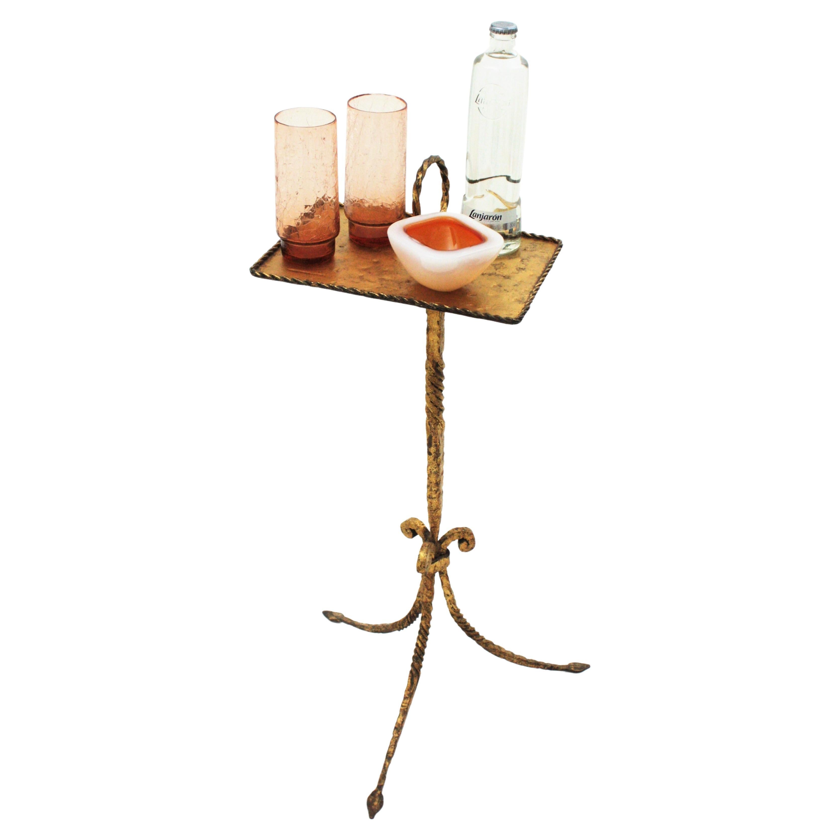 One of a kind wrought gilt iron end table with ashtray. Spain, 1940s-1950s.
This stylish hand forged iron table features a rectangular tabletop standing on a tripod base. The top has an iron twisted ring as decorative holder and an ashtray attached