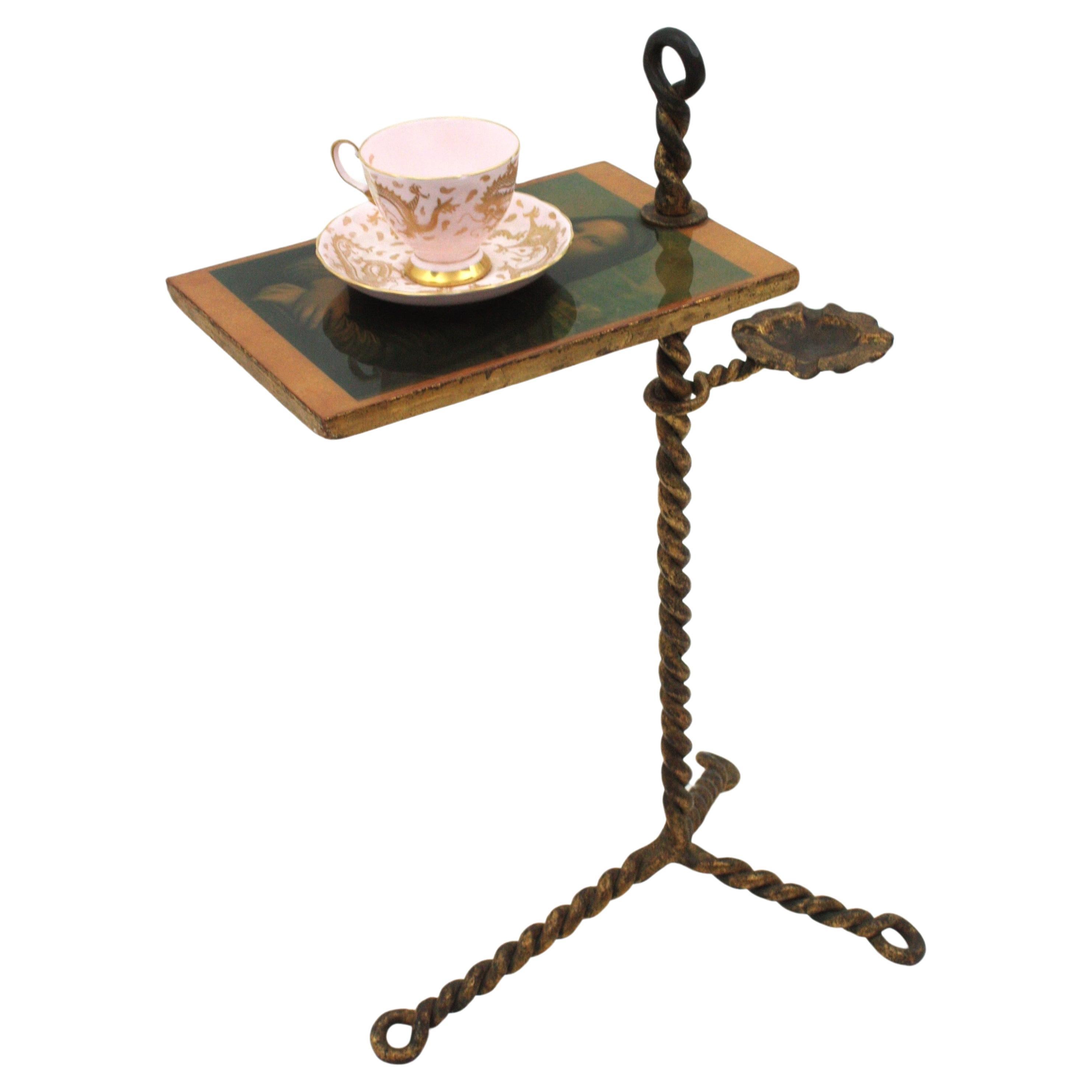 One of a kind wrought gilt iron table with ashtray with Monna Lisa print on top. Spain, 1940s-1950s.
This stylish hand forged iron table features a rectangular tabletop standing on a tripod base. The Monna Lisa is pictured on the top, it has an iron
